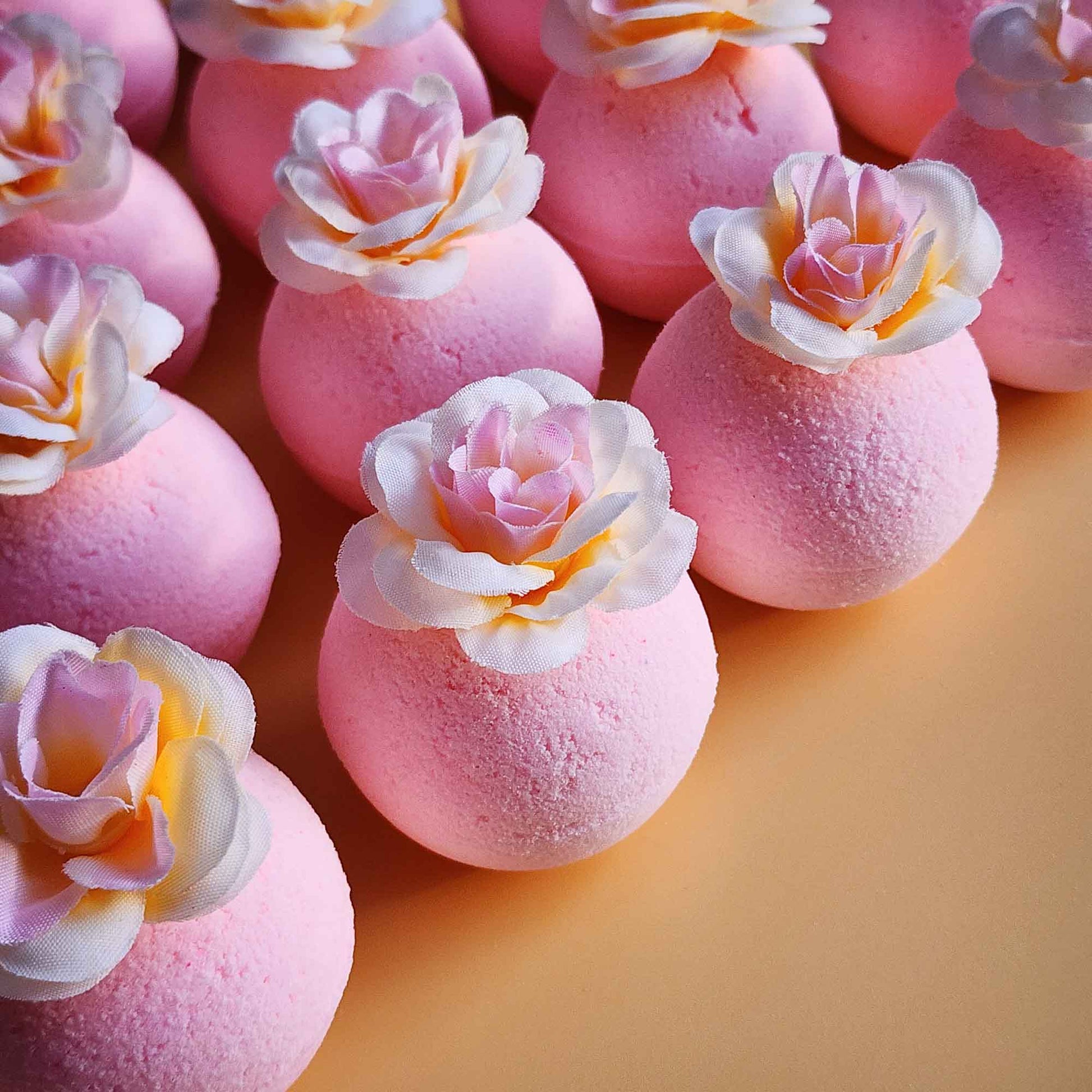 Angled view of pink magnolia bath bombs with white and blush faux petals on a soft background