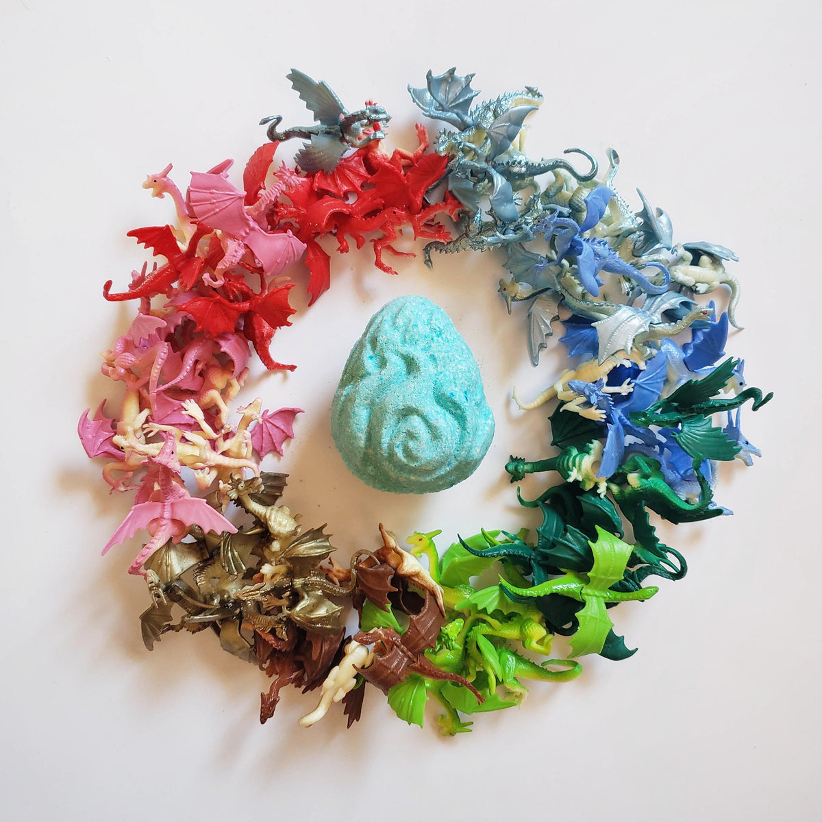 Teal bath bomb with intricate carved ridges surrounded by miniature dragon figurines