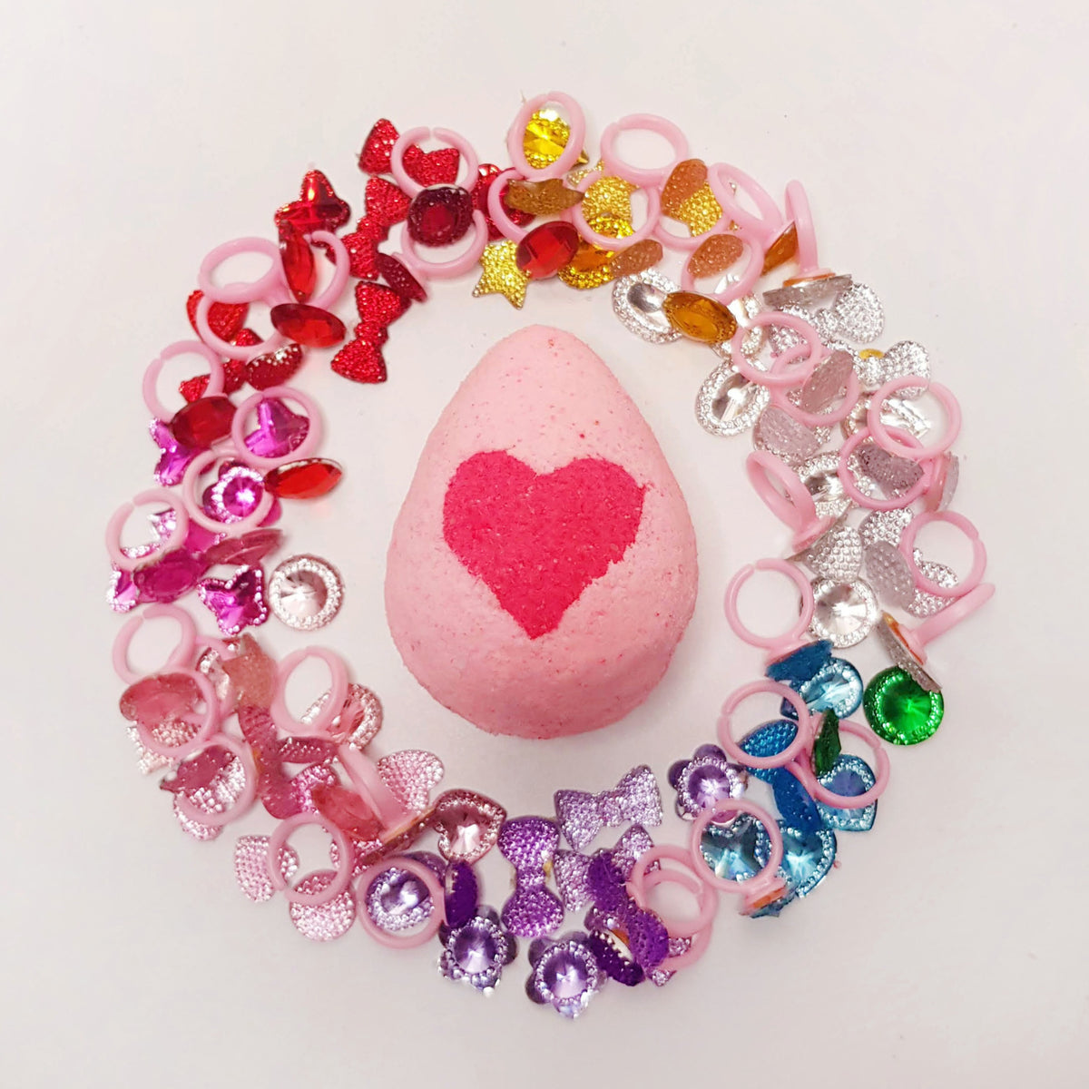 pink egg shaped bath bomb with a bright pink heart in the middle surrounded by pink bejeweled toy rings