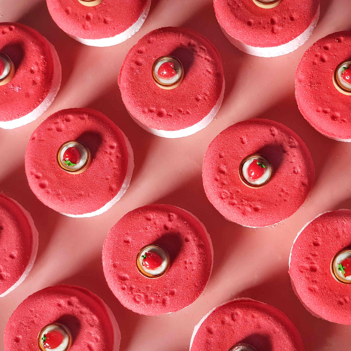 Flat disc shaped bath bombs stacked and placed in a tidy array on a plain pink background