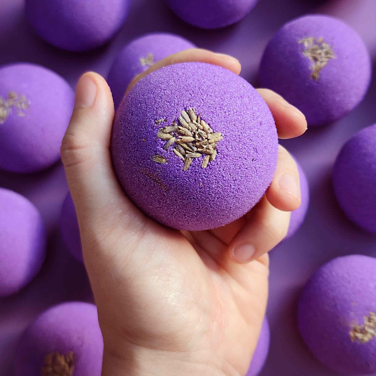 Hand holding a Relax bath bomb in front of matching purple bath bombs