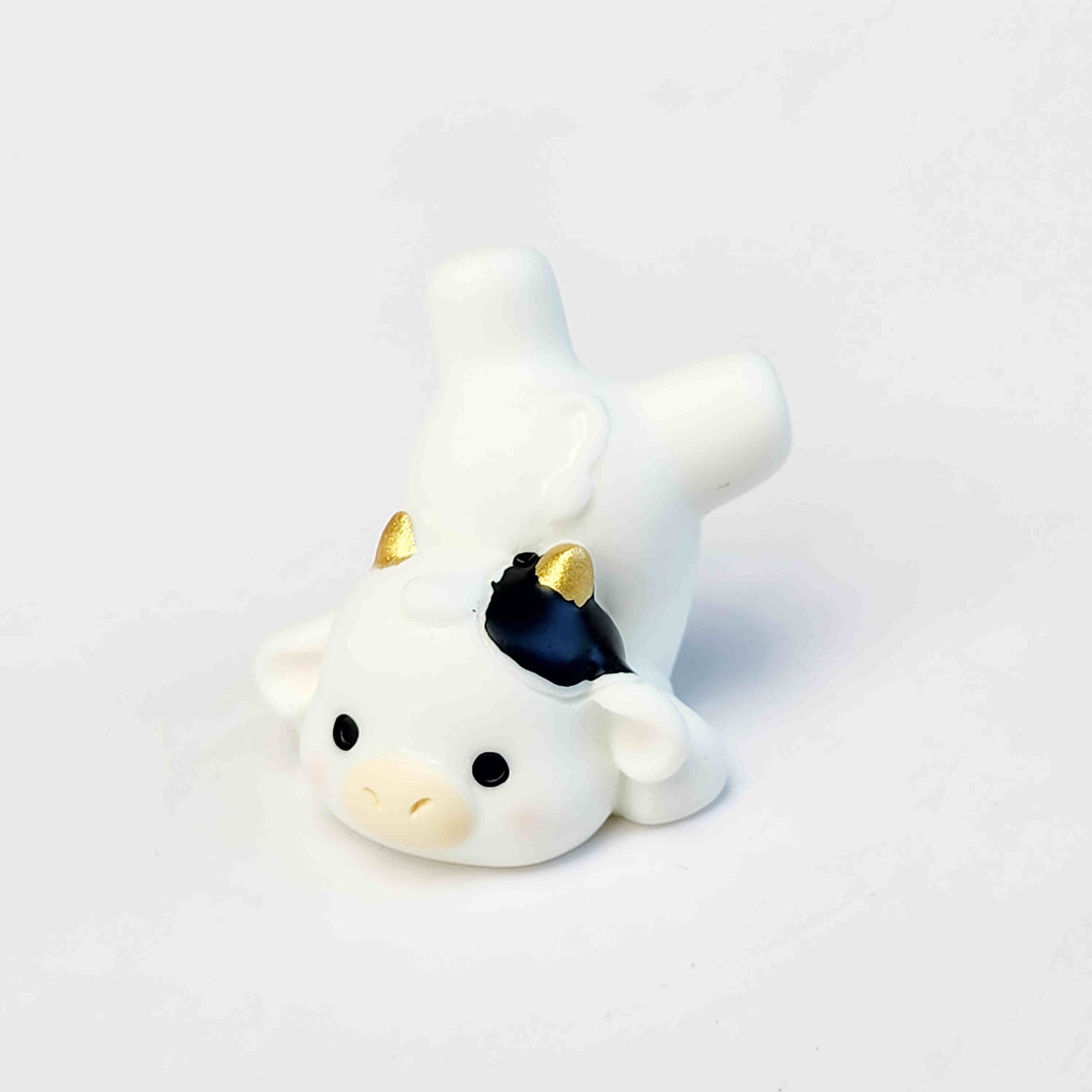 flopped over cute cow figurine with gold horns on a white background
