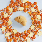 Croissant bath bomb centered in a ring of miniature bread toys
