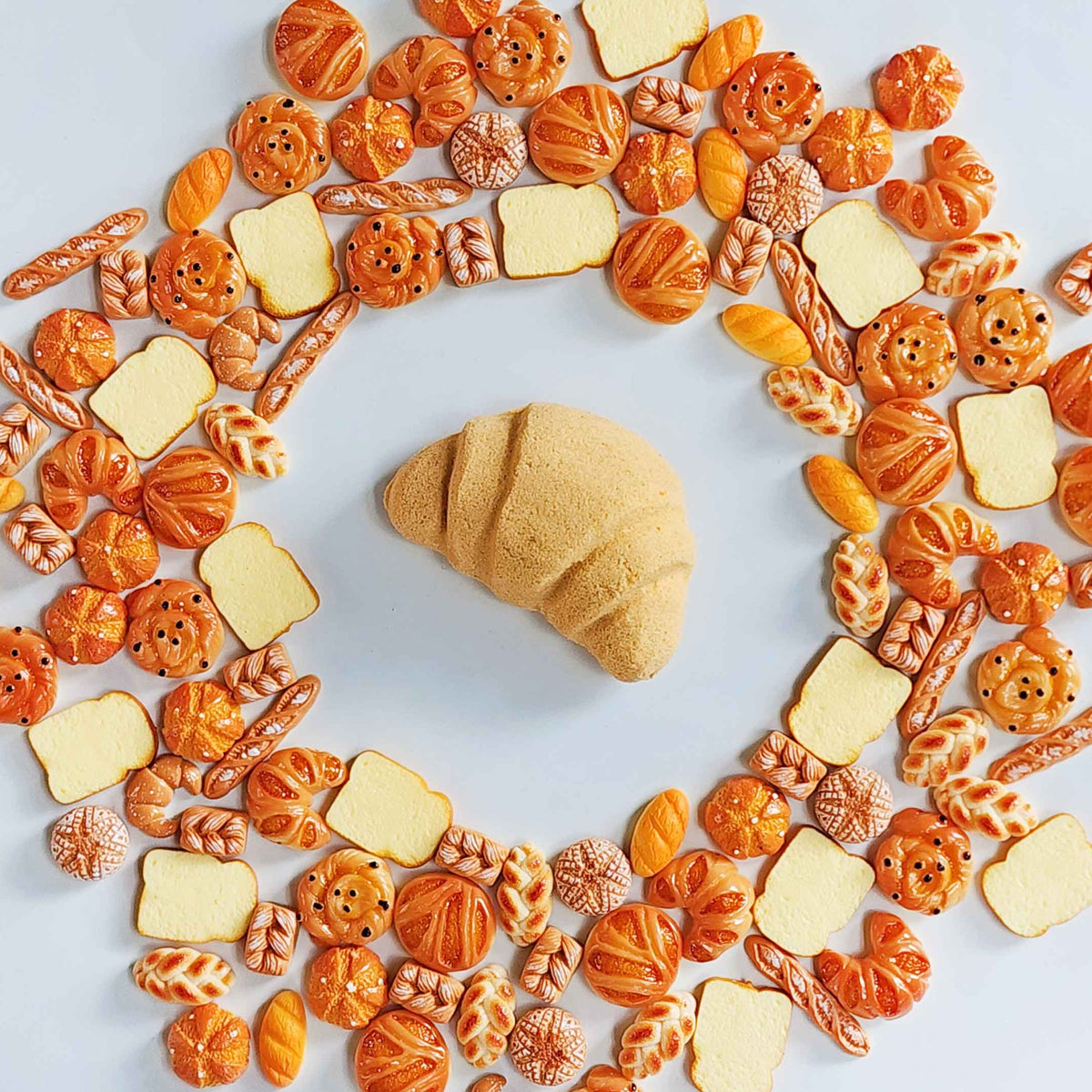 Croissant bath bomb centered in a ring of miniature bread toys