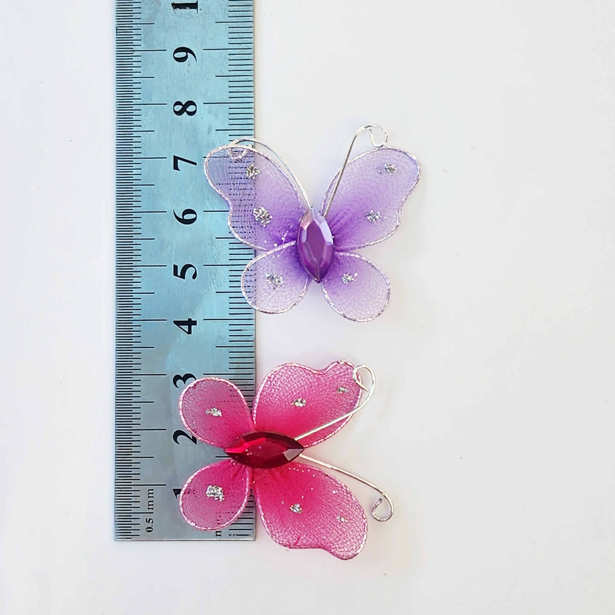 measurements of a pink and purple butterfly made of mesh fabric and wire being held in a hand on a white background