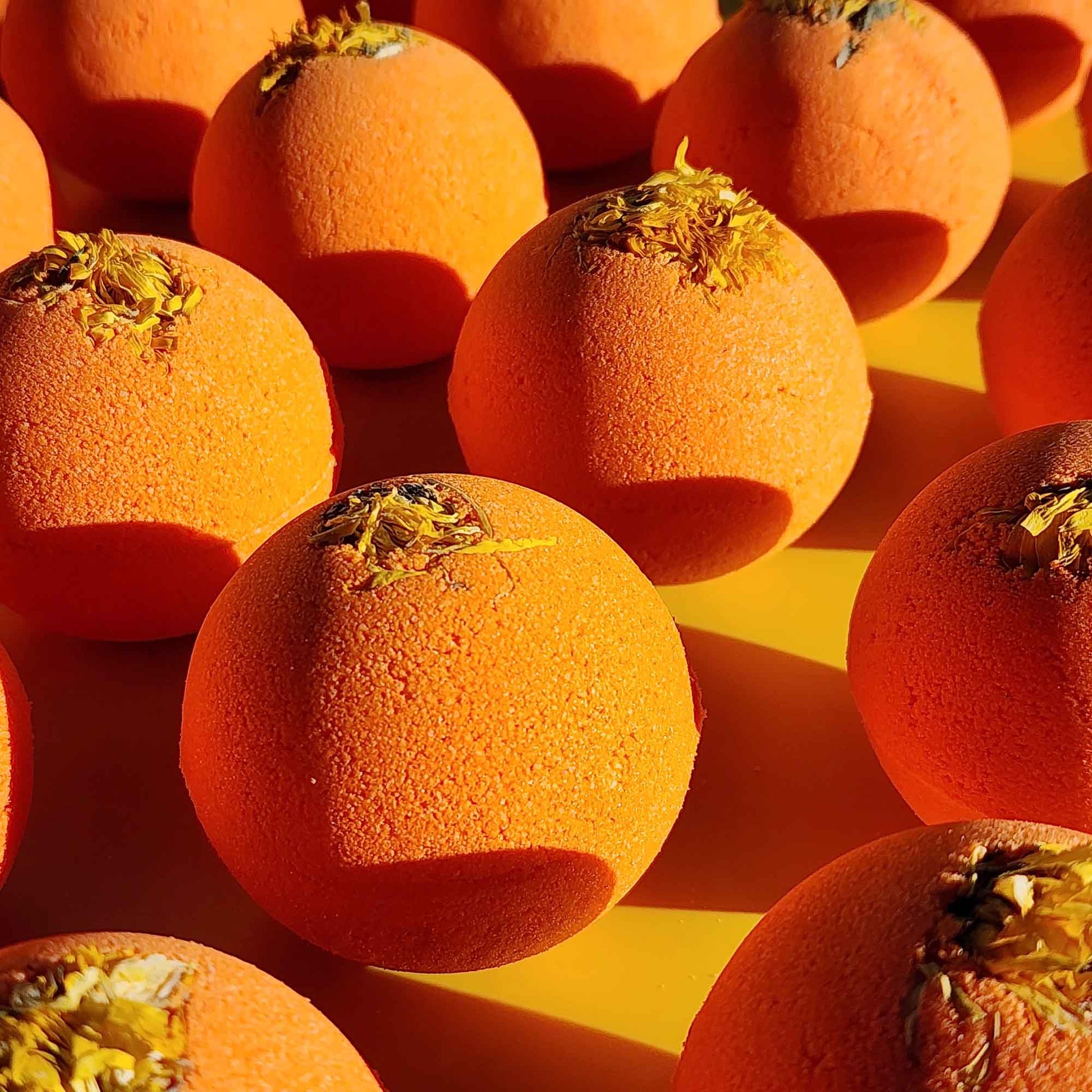 right orange Restore aromatherapy bath bombs topped with whole chrysanthemum flowers on a yellow surface