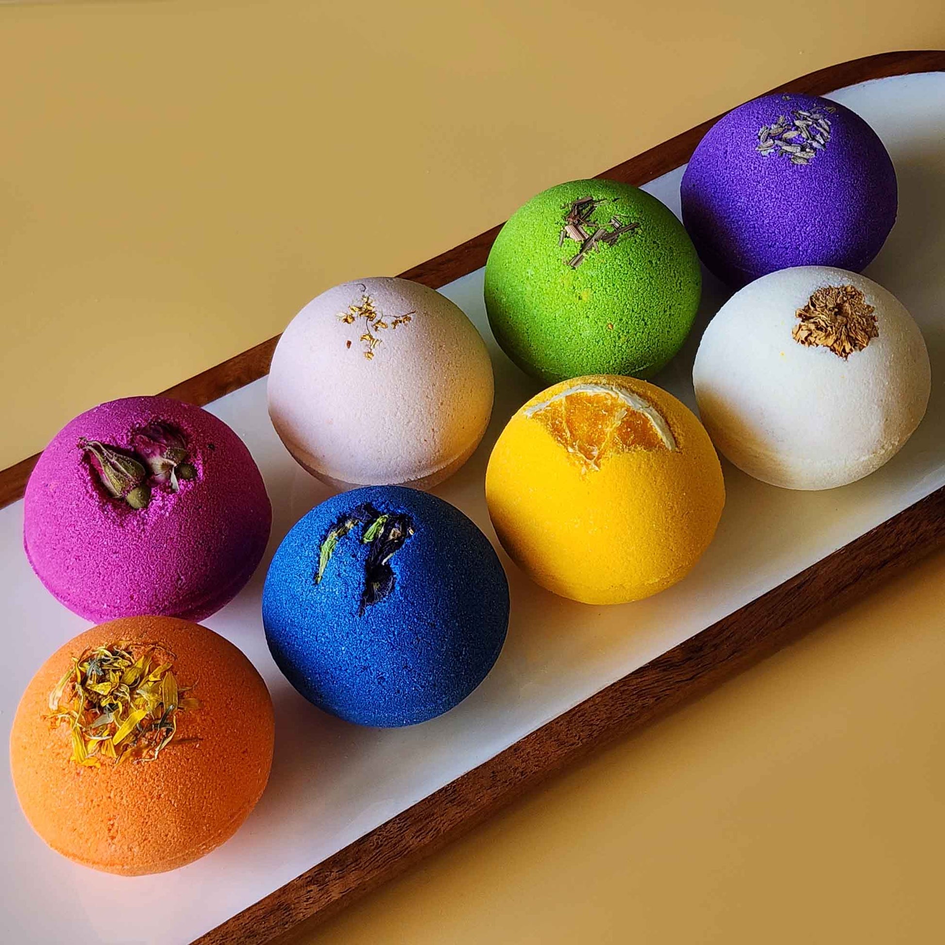 Eight colorful aromatherapy bath bombs arranged on a wooden tray