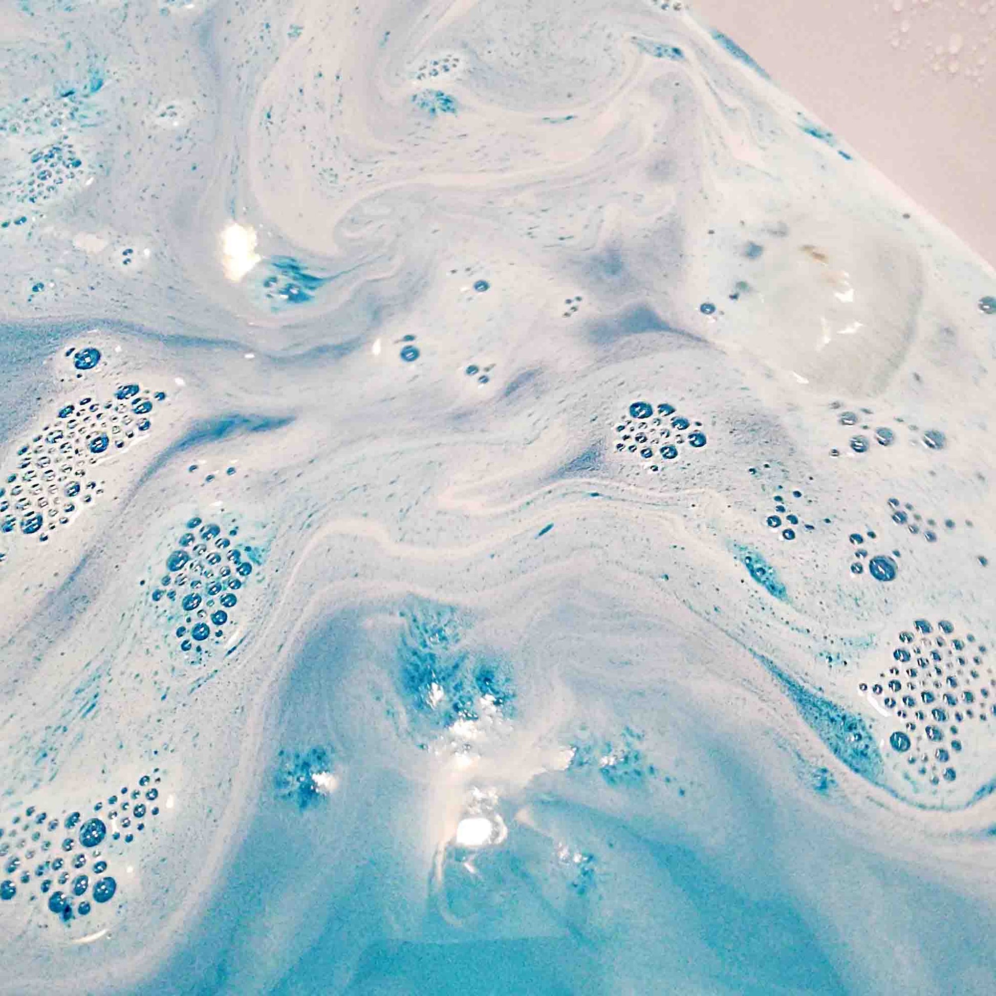 teal blue bath bomb dissolving in a bath turning the water a lush blue