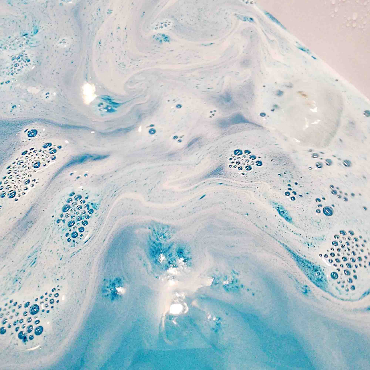 teal blue bath bomb dissolving in a bath turning the water a lush blue
