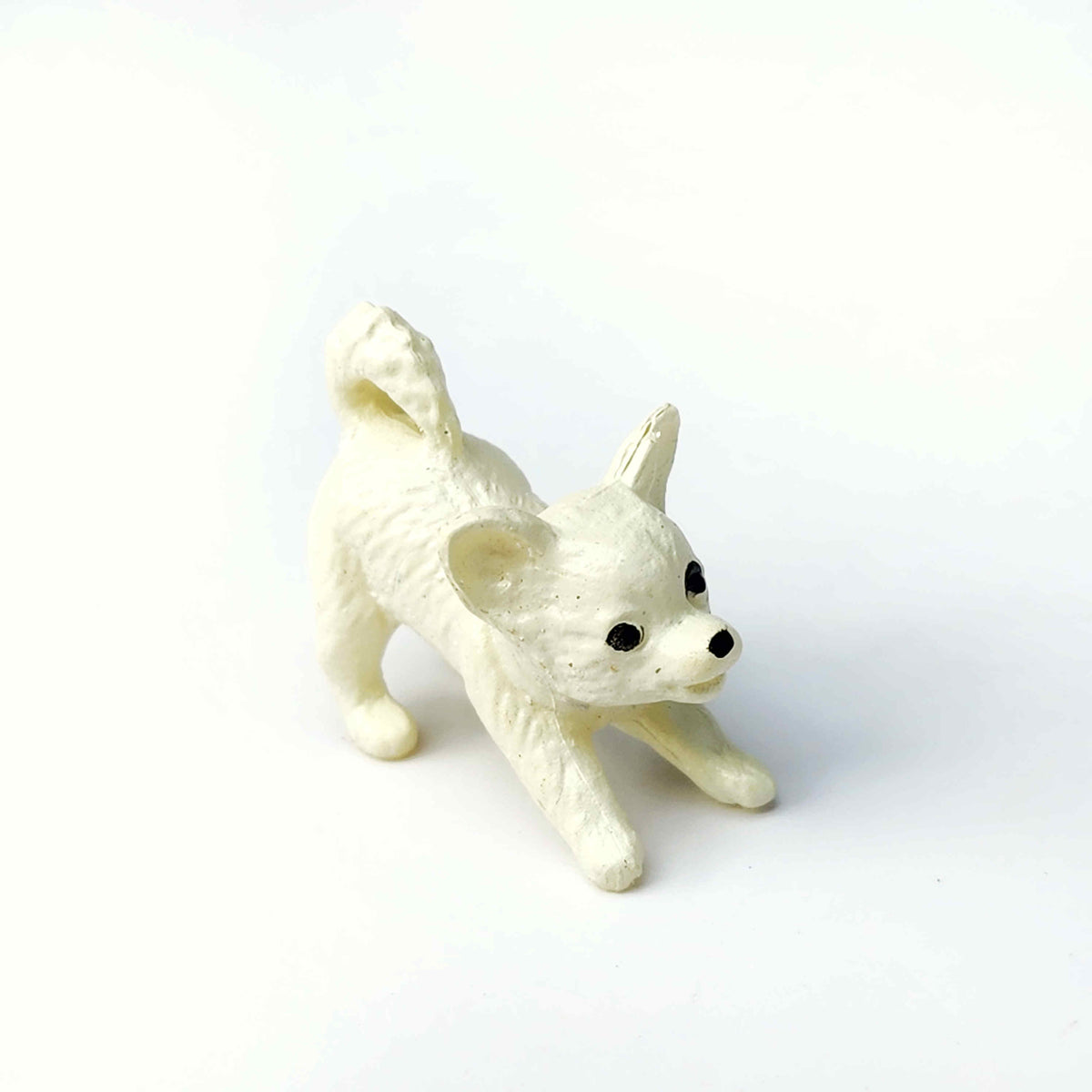 a PVC figurine of a white chihuahua stretching on a white background