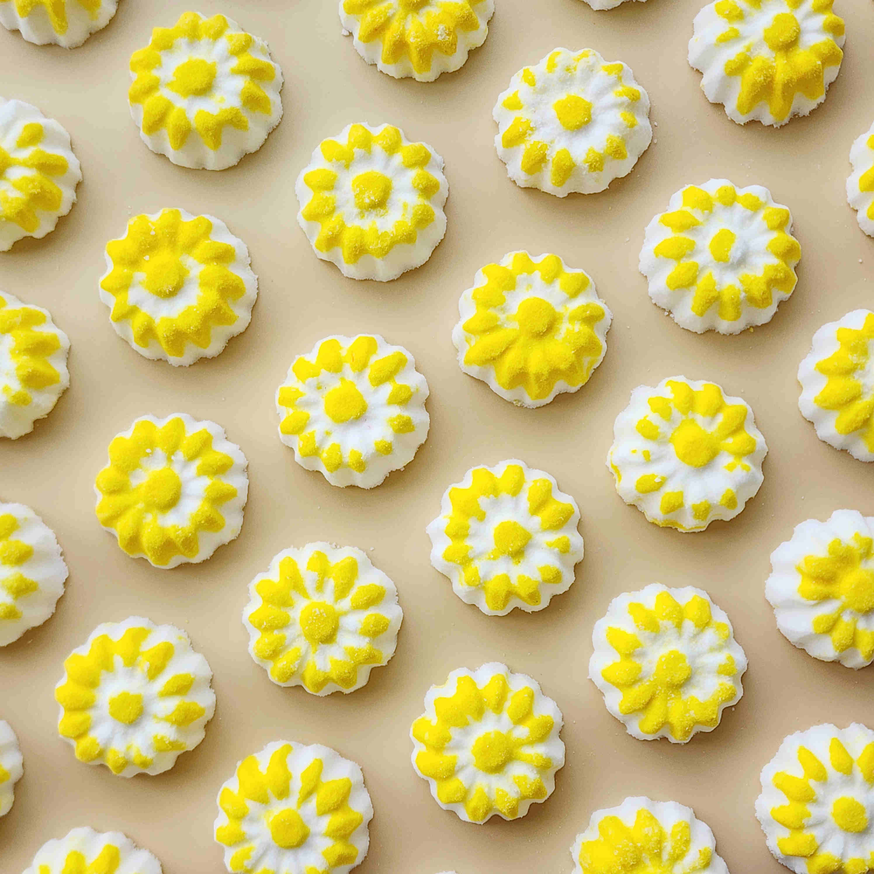 chamomile shaped mini bath bombs with a white base and yellow detail on a neutral plain background