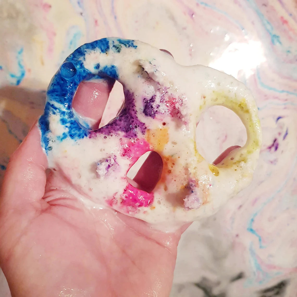 Pretzel bath bomb in water with rainbow embeds