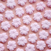 5 petal cherry blossom shaped bath bombs coloured light pink on a plain pink background