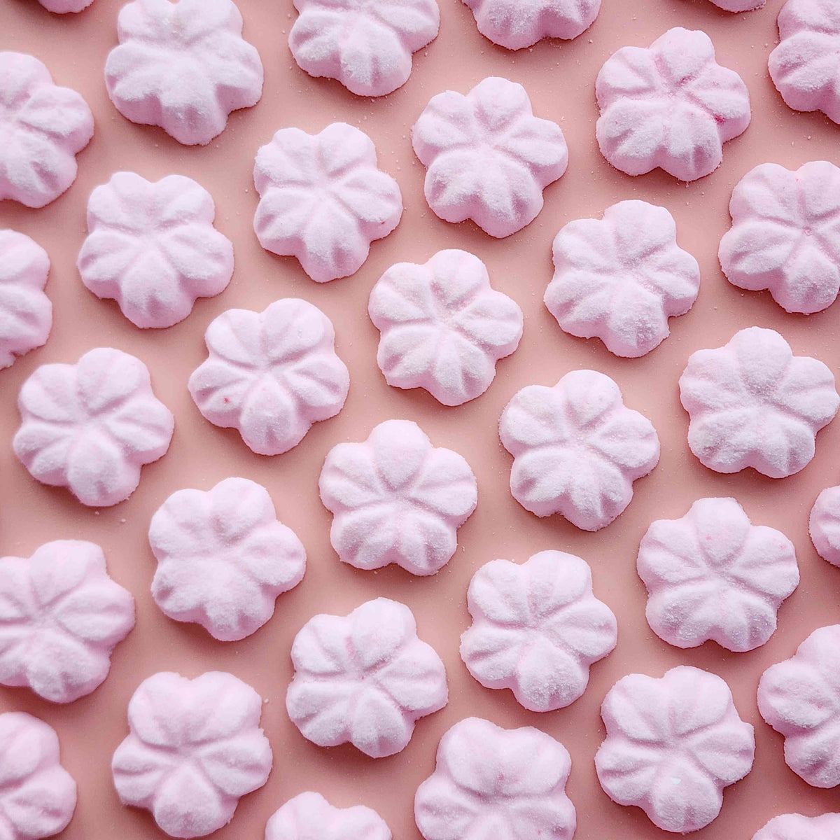 5 petal cherry blossom shaped bath bombs coloured light pink on a plain pink background