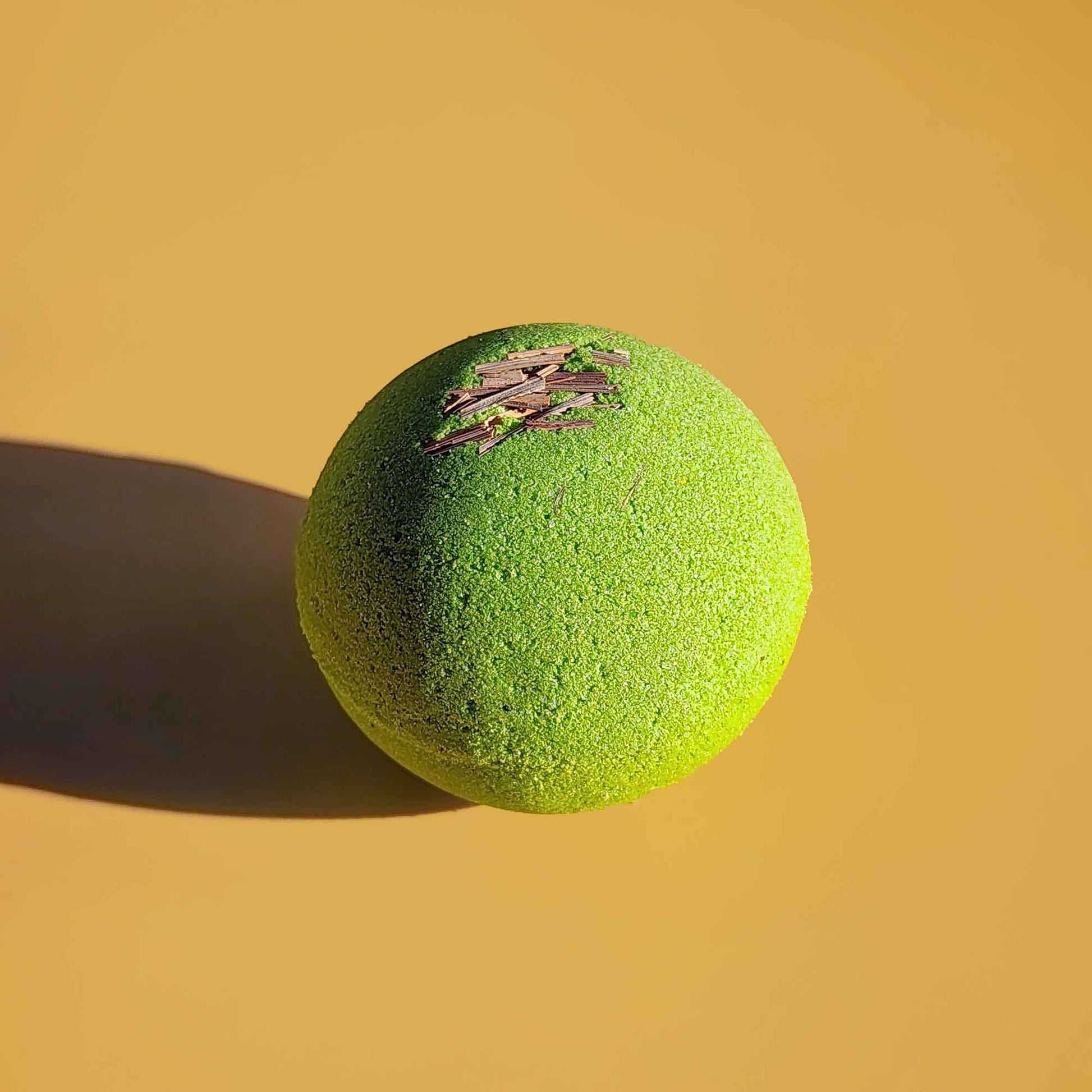Close-up of a single bright green Repair aromatherapy bath bomb with dried lemongrass on a yellow surface