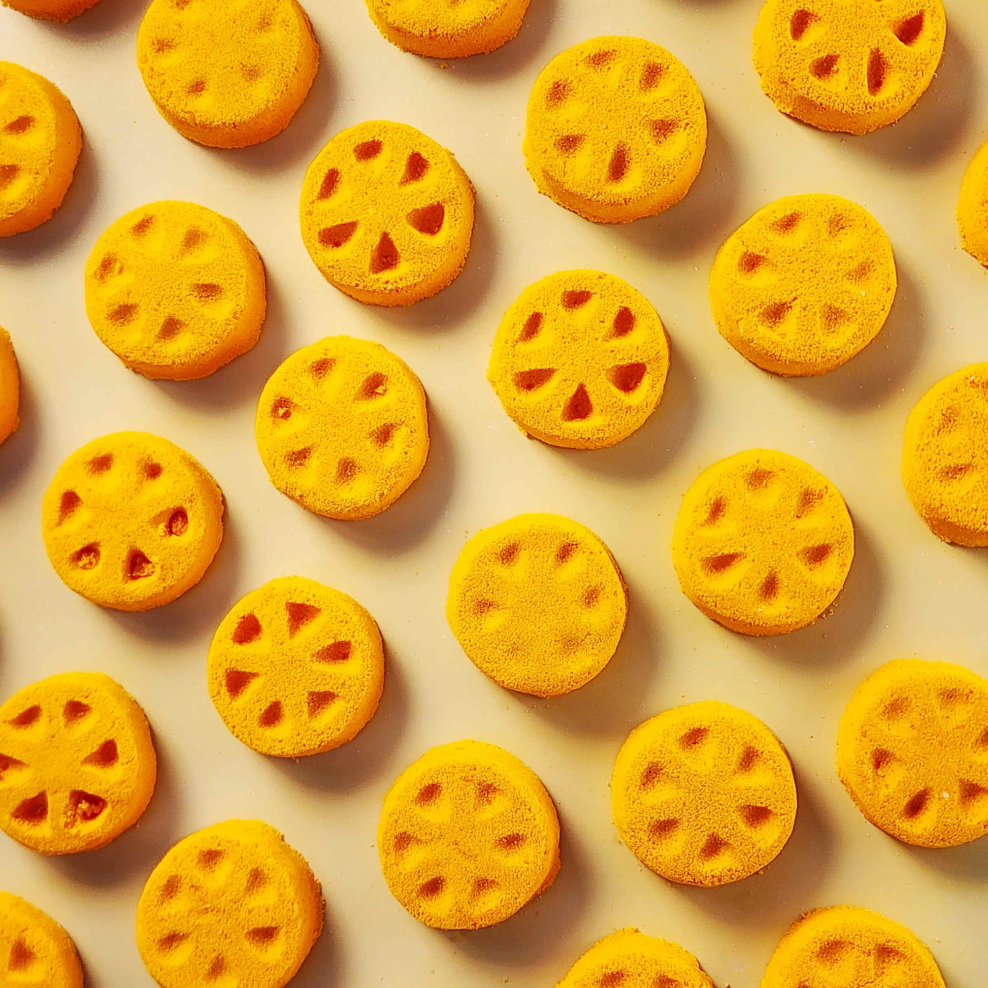 Orange slice shaped mini bath bomb layed out in an array across a plain neutral background