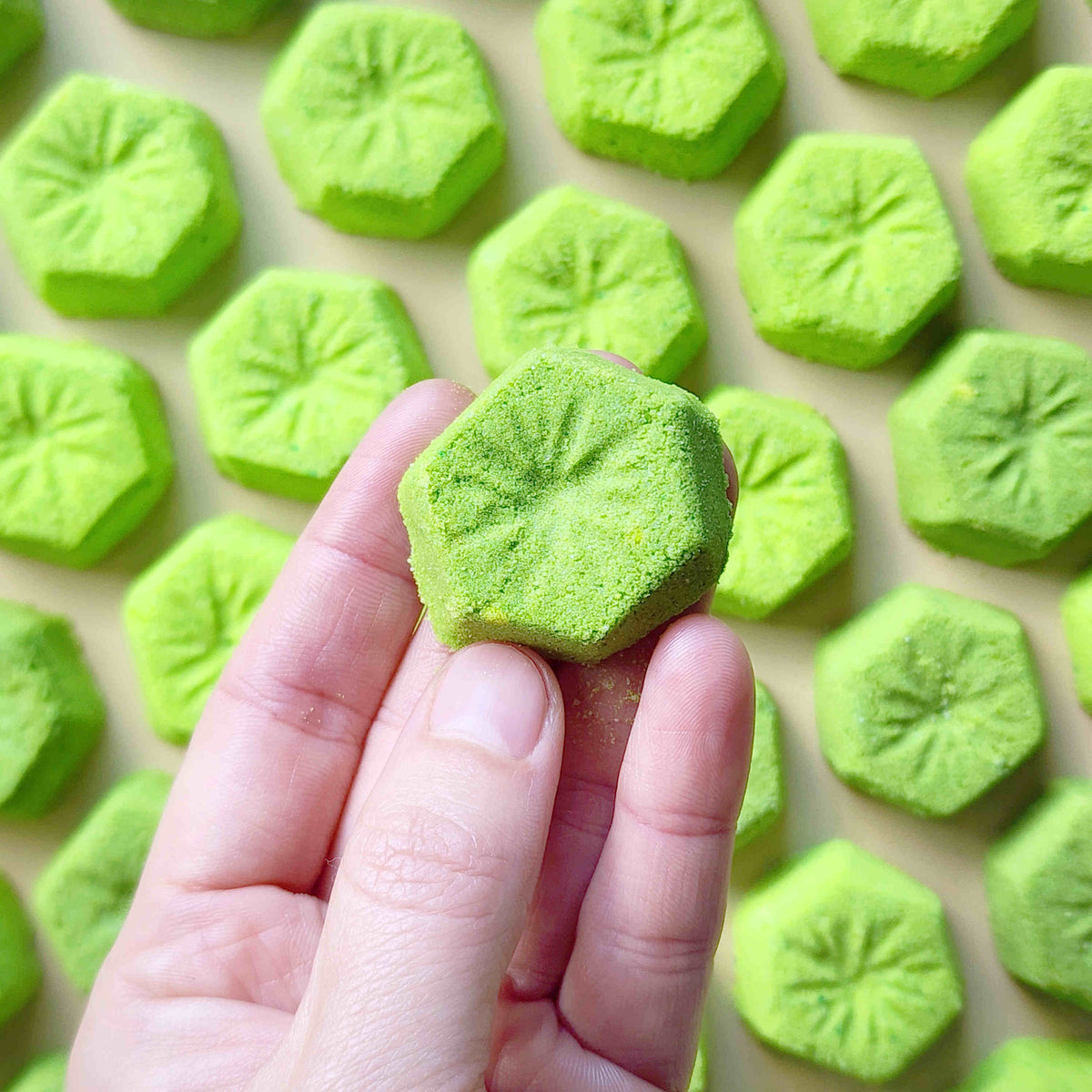 Hand holding a green kiwi-slice mini bath bomb