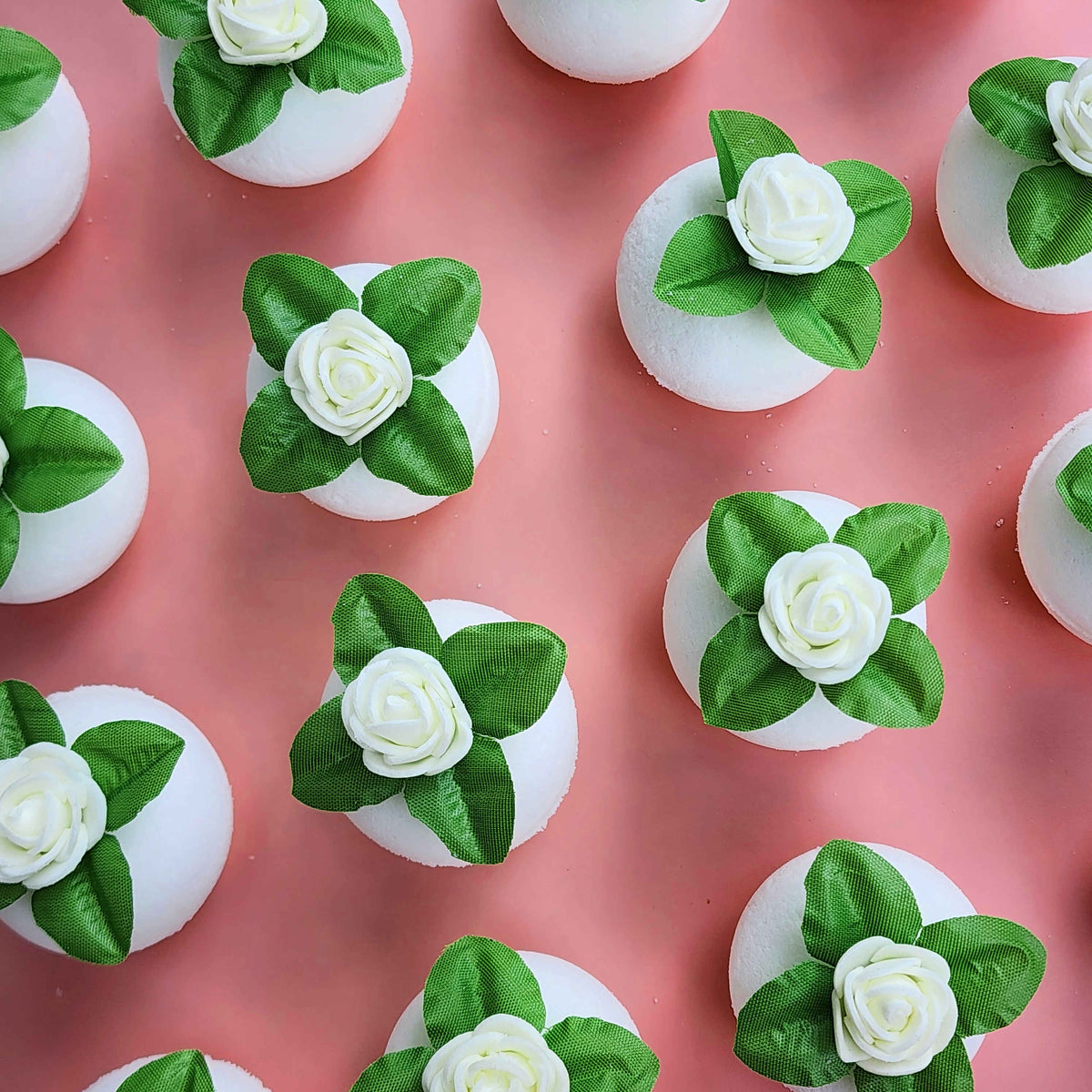 round white bath bombs with jasmine flowers on top over a pink background