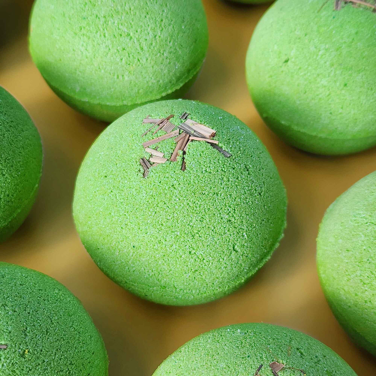 Multiple bright green Repair aromatherapy bath bombs topped with small pieces of dried lemongrass on a warm yellow background