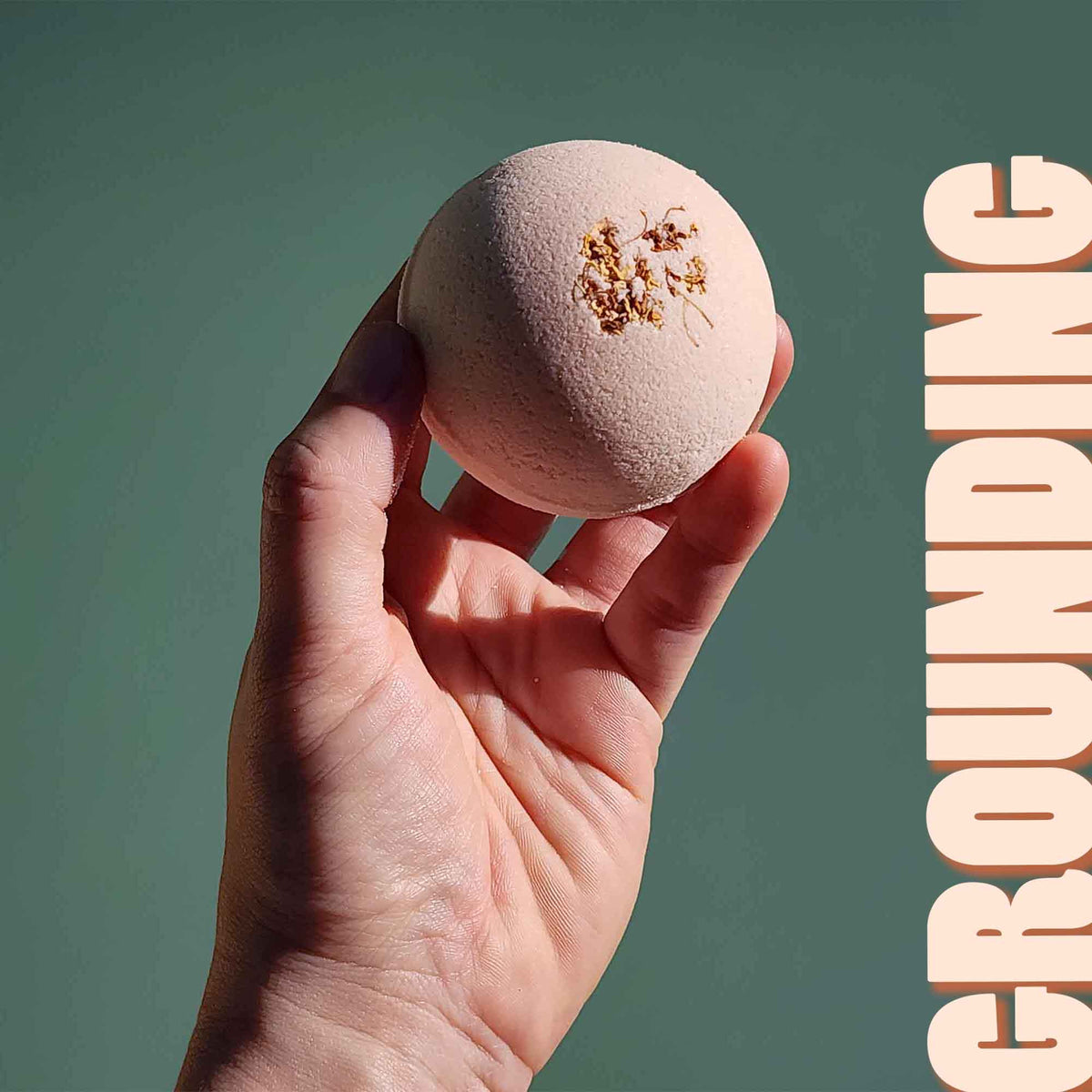 Hand holding the pale pink Grounding aromatherapy bath bomb
