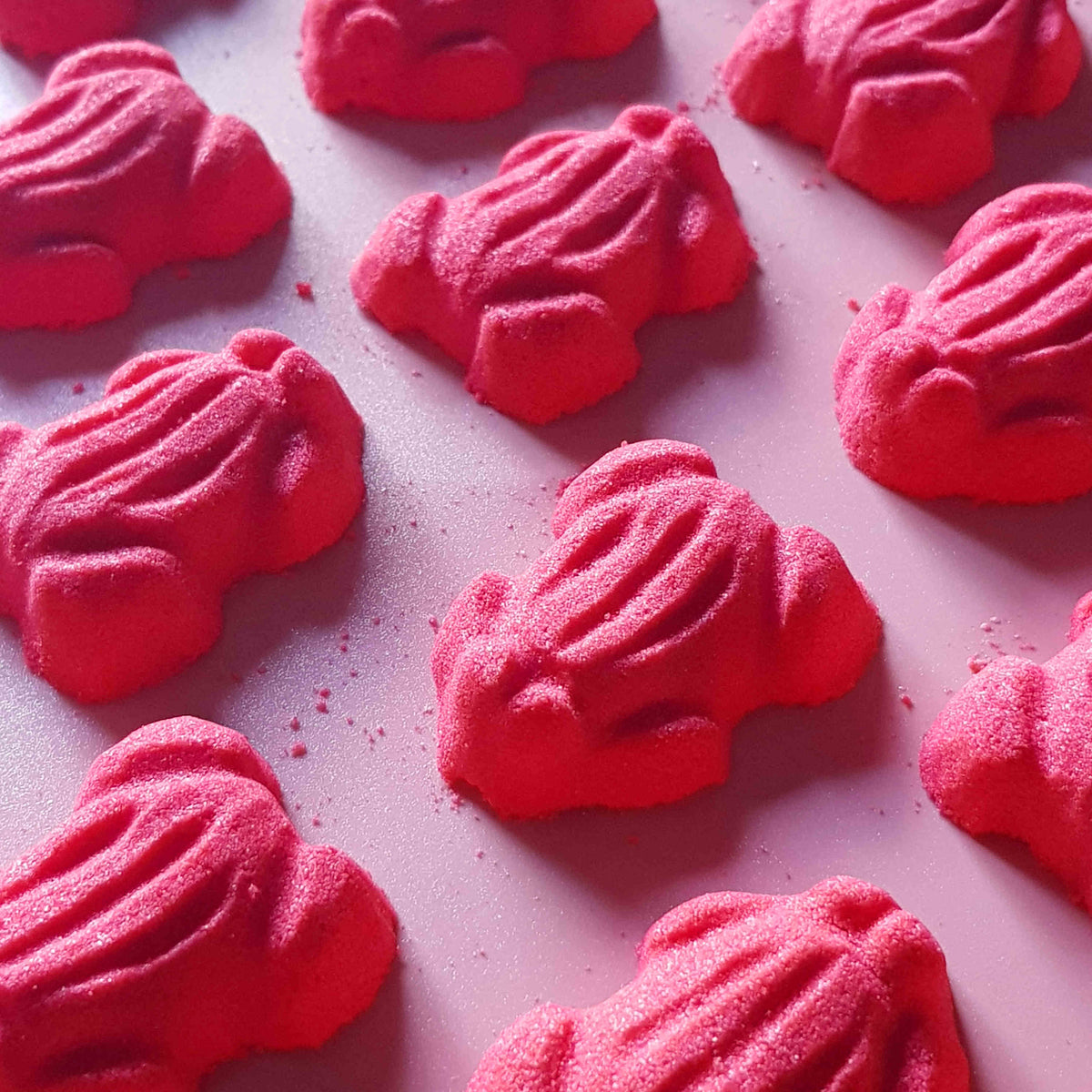 Red frog gummy candy shaped bath bombs layed out in an array over a plain red background