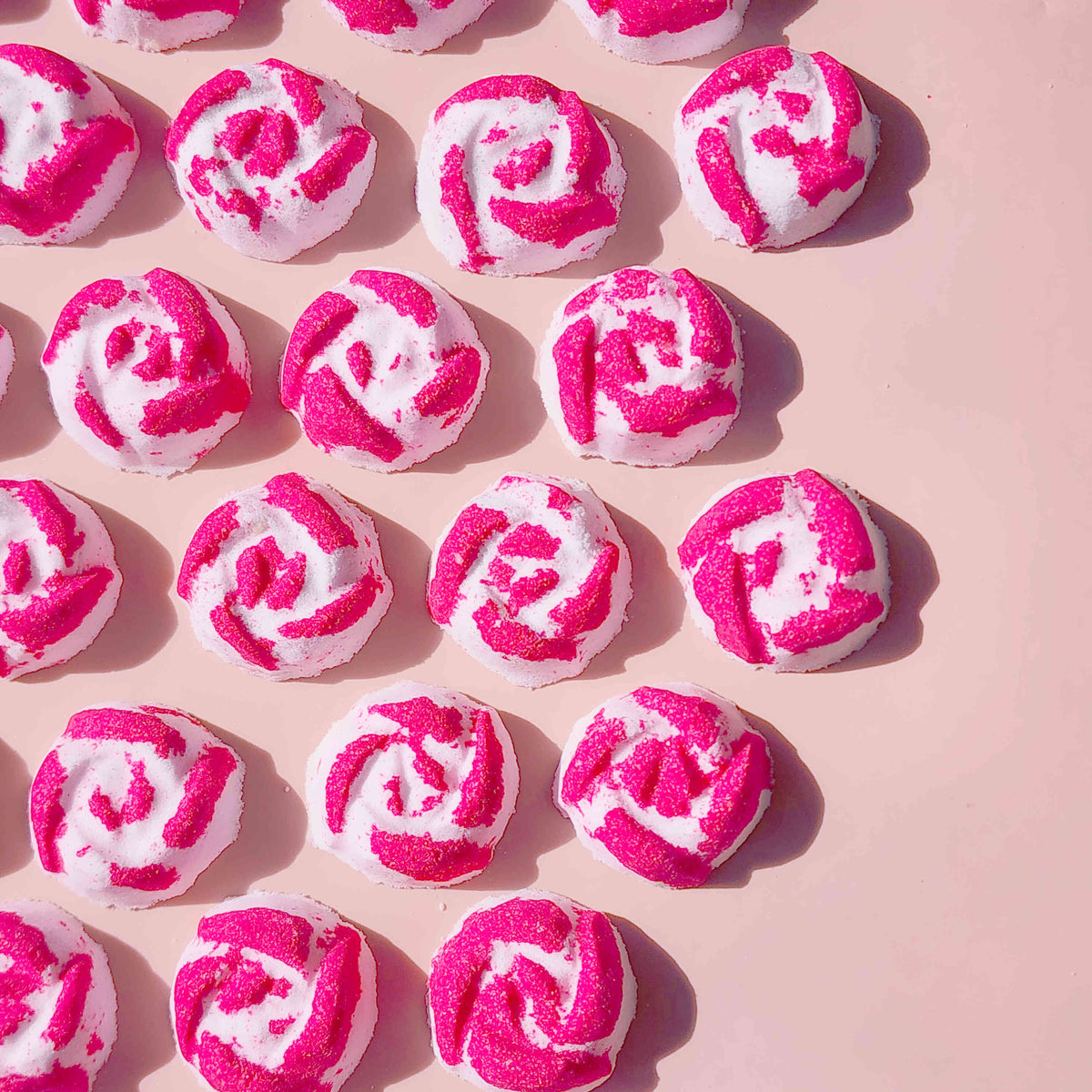 Rows of pink and white Peony Rose mini bath bombs on a pink background