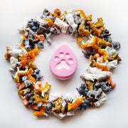 pink fat egg shaped bath bomb with a cat paw print embossed in the centre surrounded by miniature cat figurines