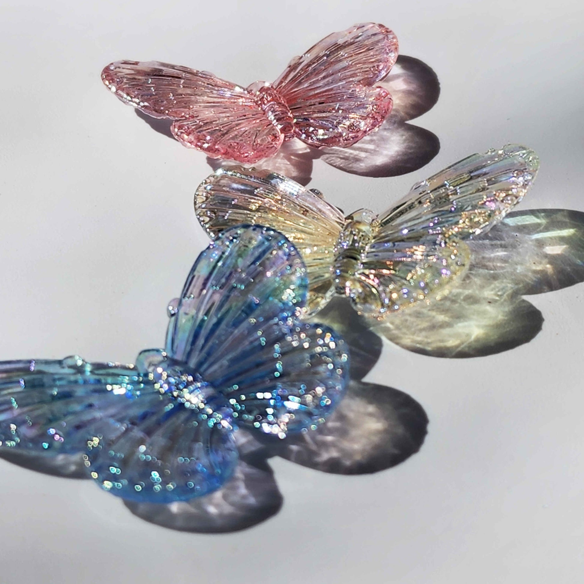 three colour tinted clear butterfly charms refracting light on a white background