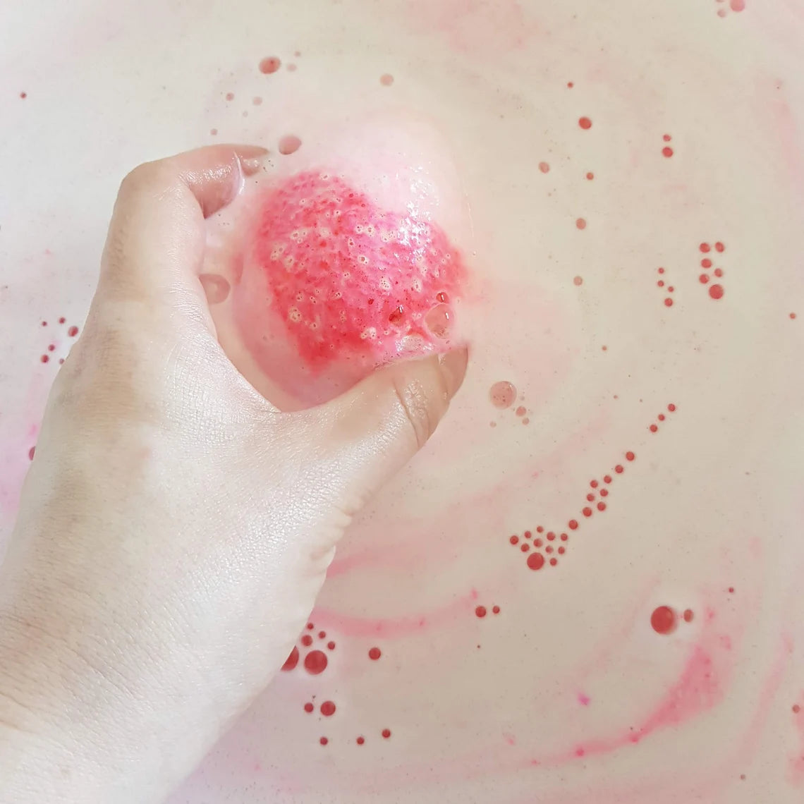pink egg shaped bath bomb with a bright pink heart in the middle being held in water bubbling