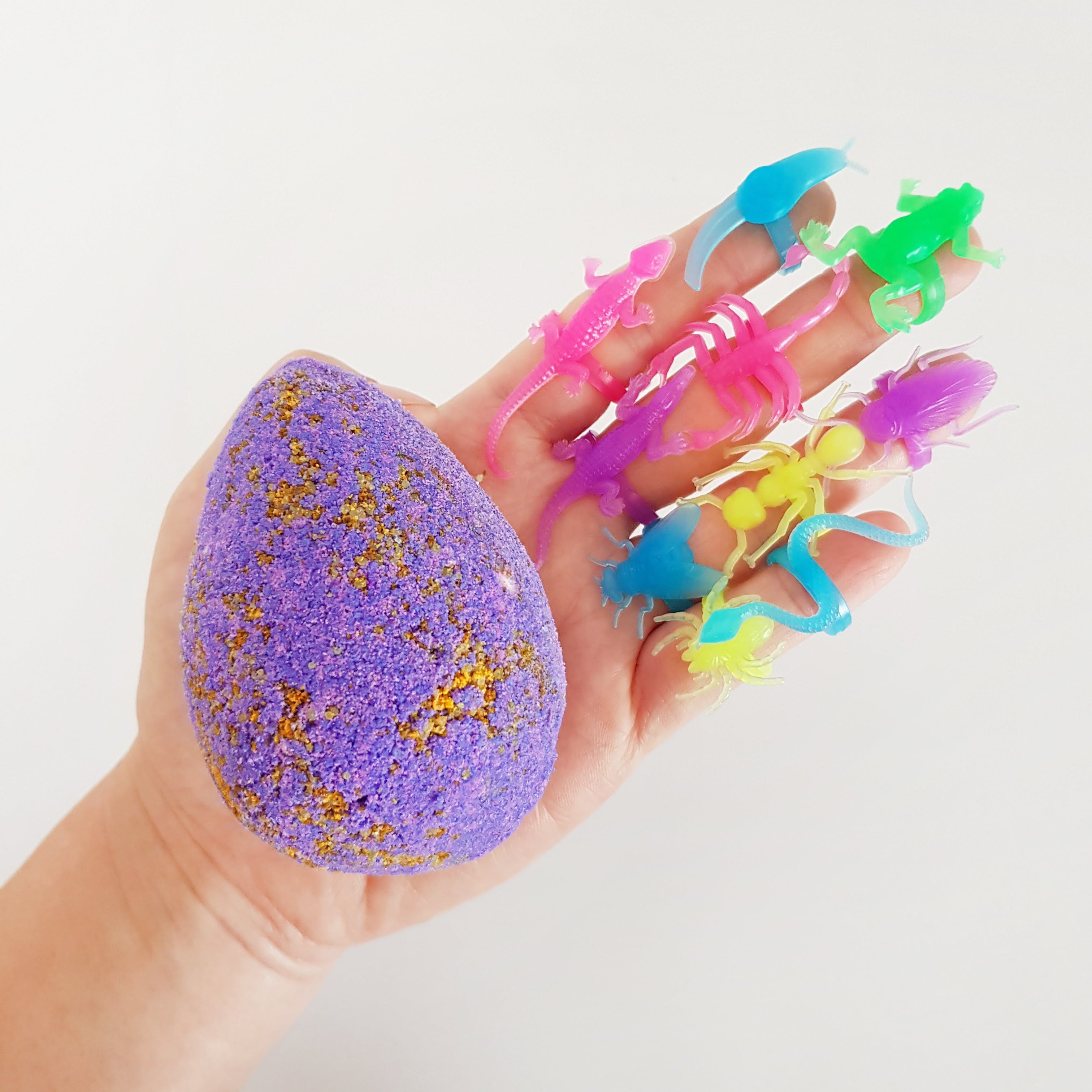 bright purple egg shaped bath bomb held in a hand with neon glow in the dark insect themed toy rings