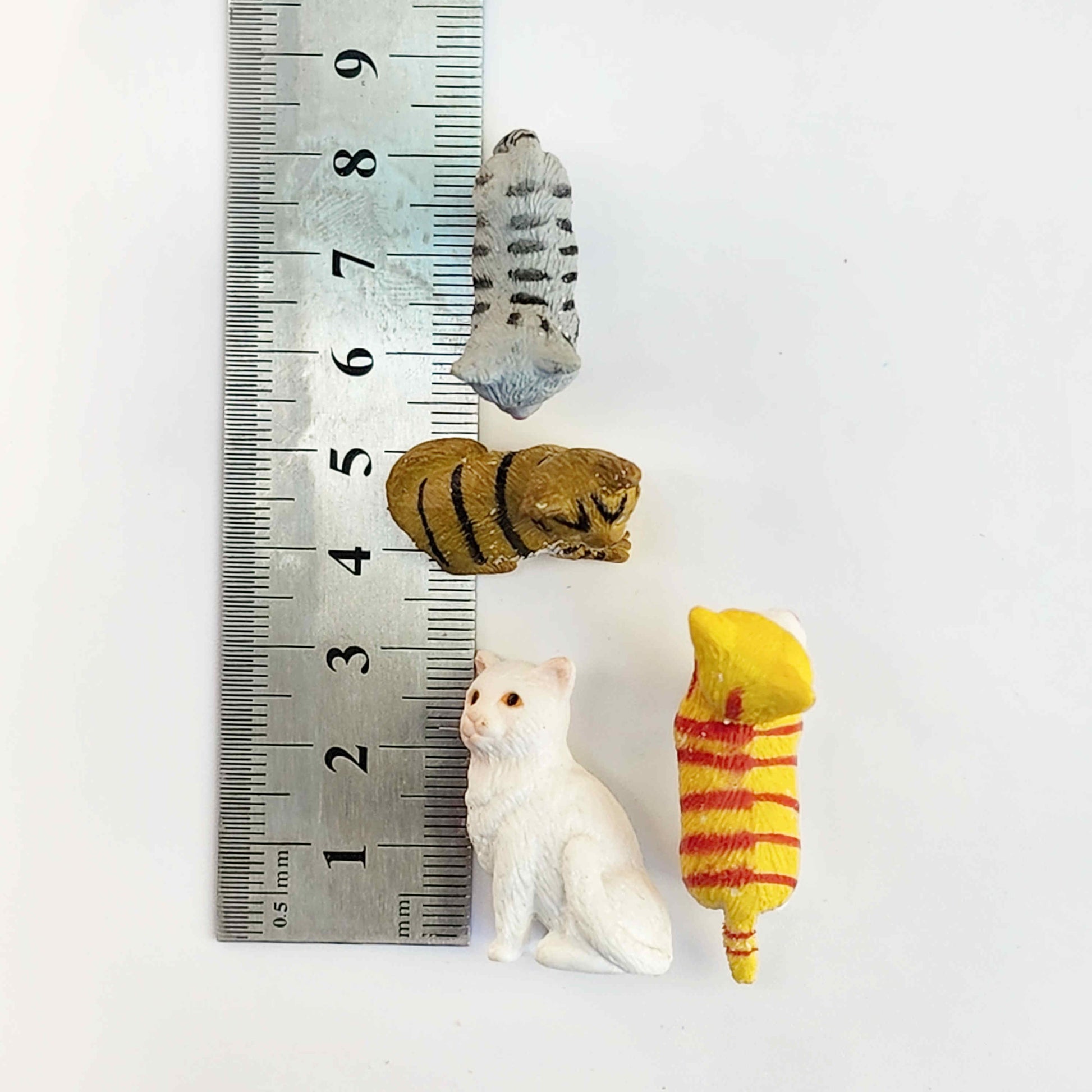measurements of pvc cat figurines with a metal ruler on a white background