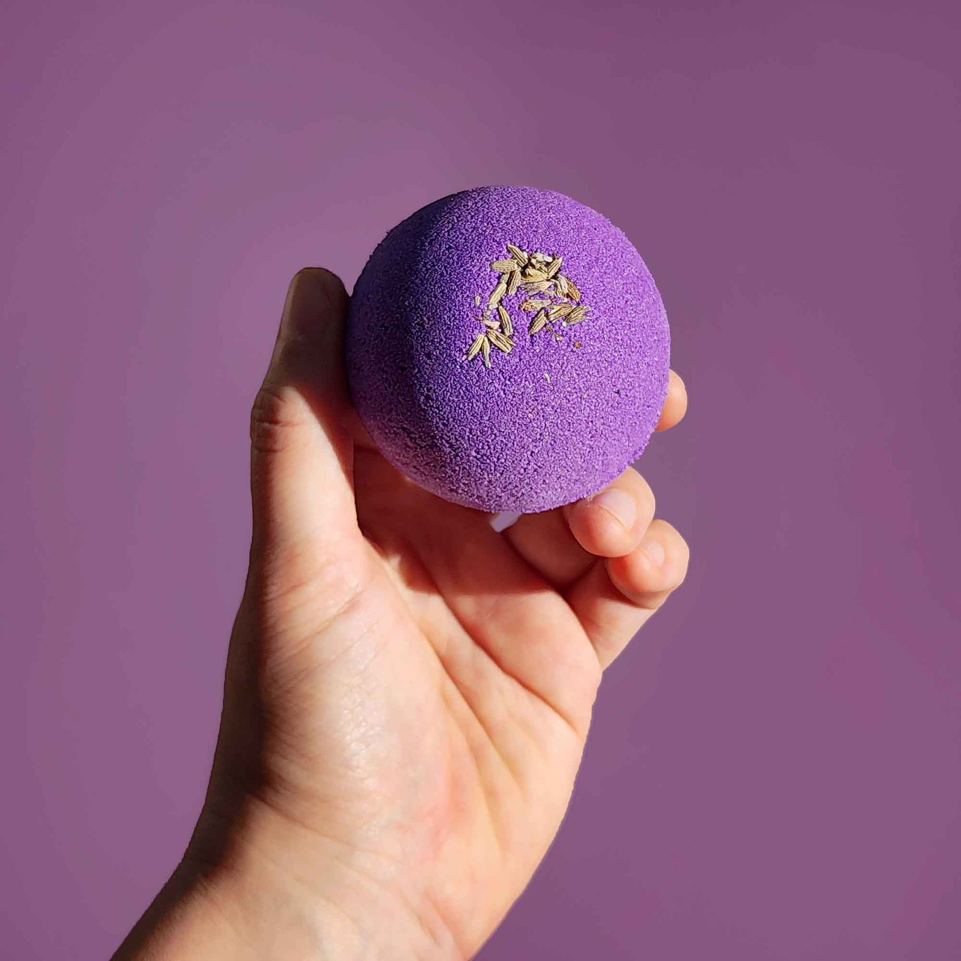 Hand holding a purple Relax aromatherapy bath bomb