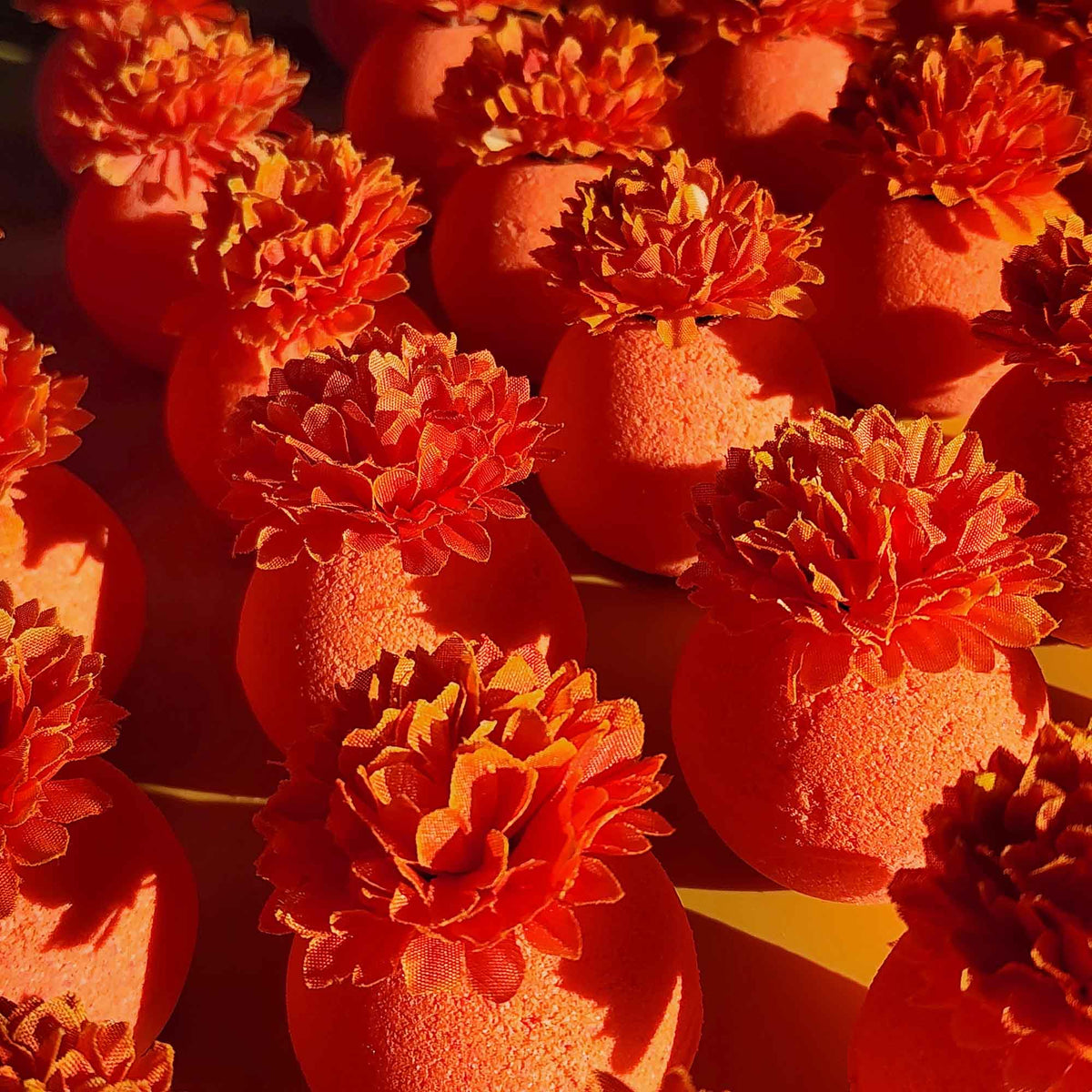 Warm light highlighting textured orange bath bombs topped with detailed calendula blooms