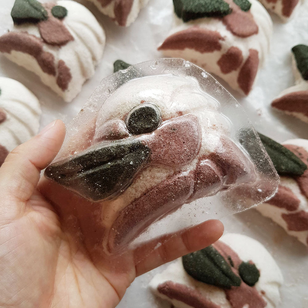 Hand holding a Paperbark Kookaburra bath bomb inside a clear plastic mold, with matching bath bombs behind