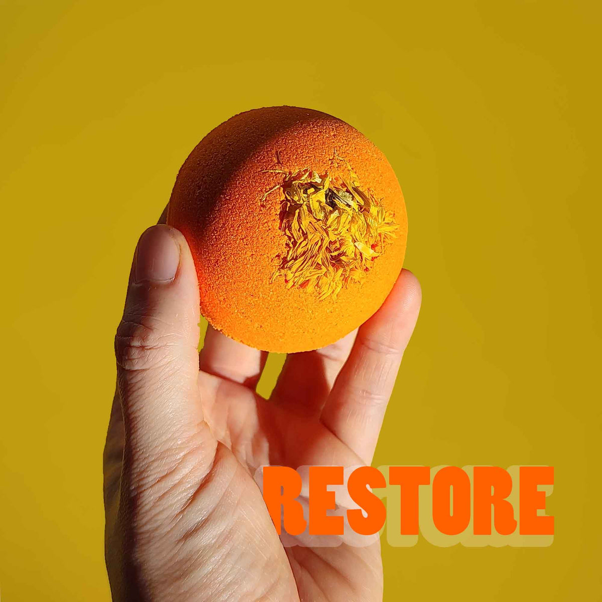 Hand holding the orange Restore aromatherapy bath bomb