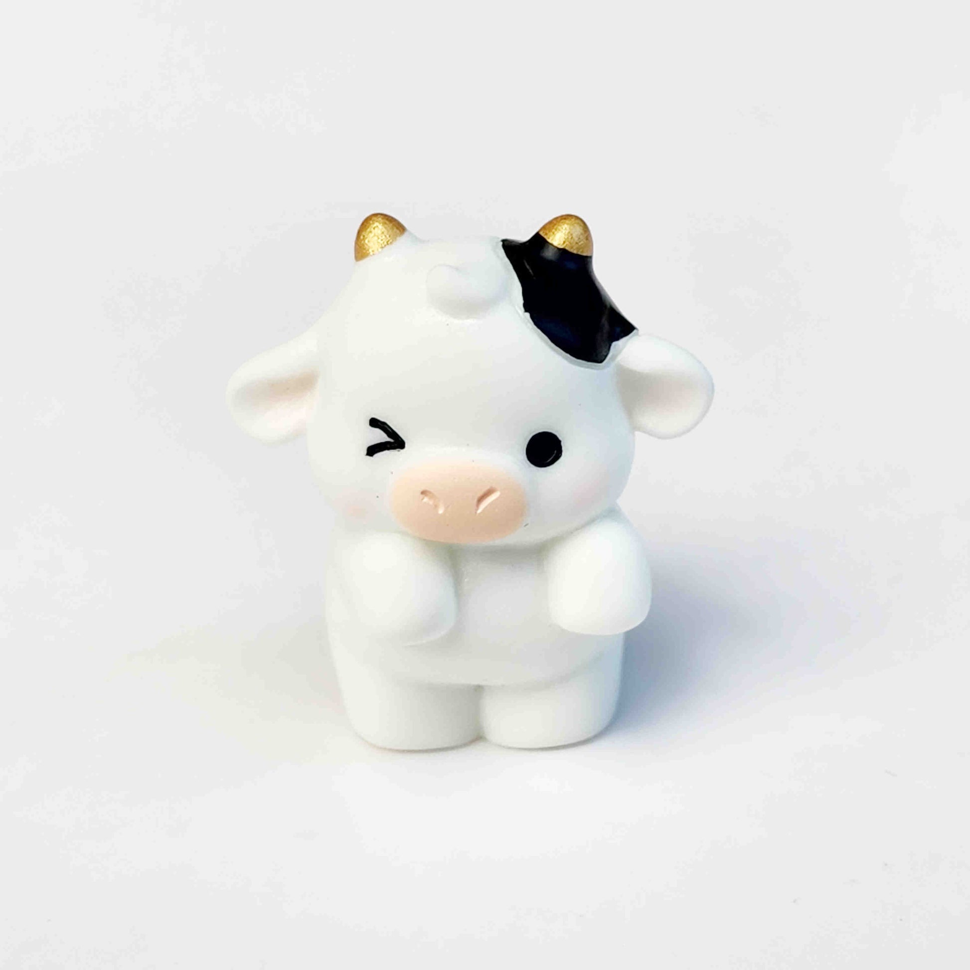 standing and winking cute cow figurine with gold horns on a white background