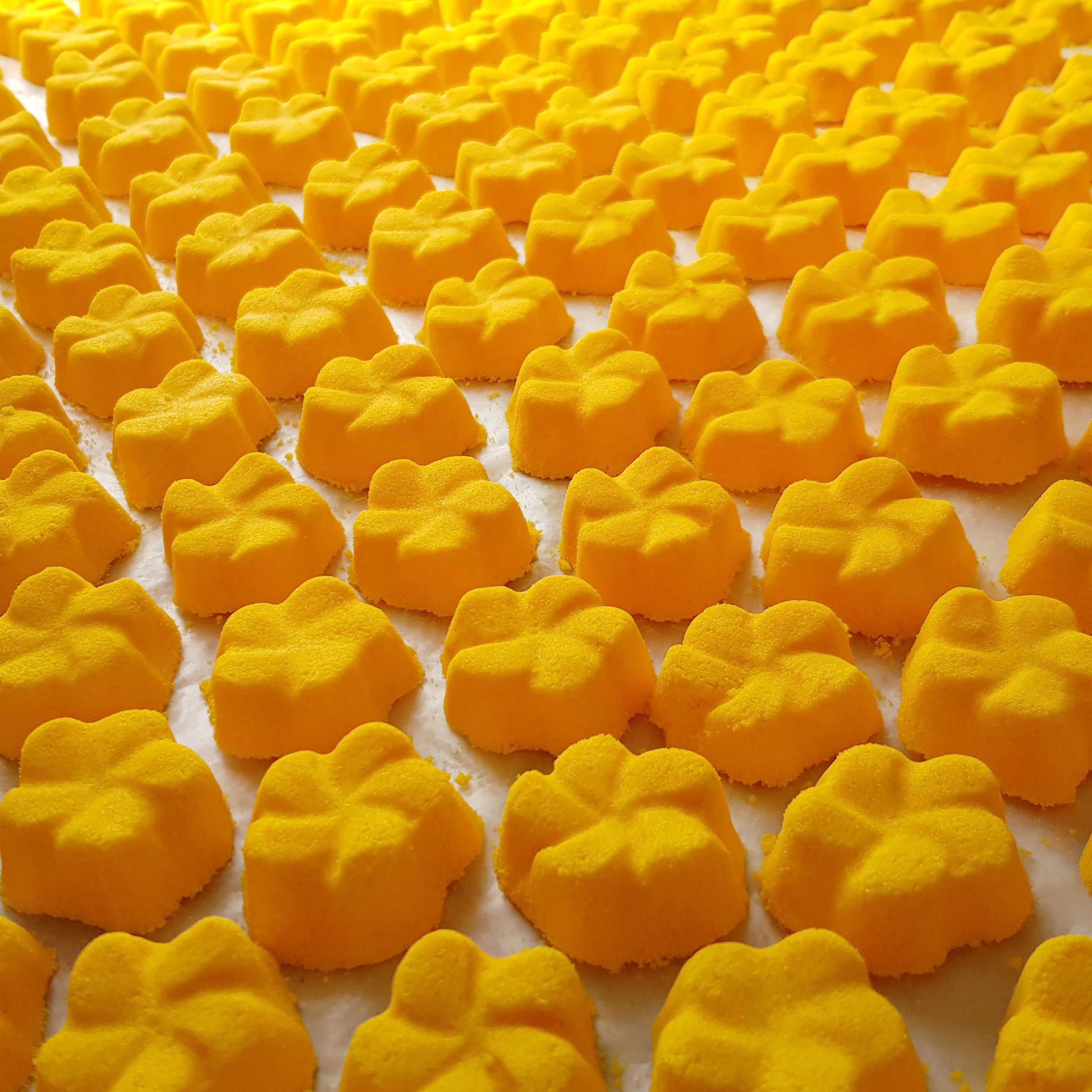 yellow frangipani shaped bath bombs placed in a neat array on a plain white background