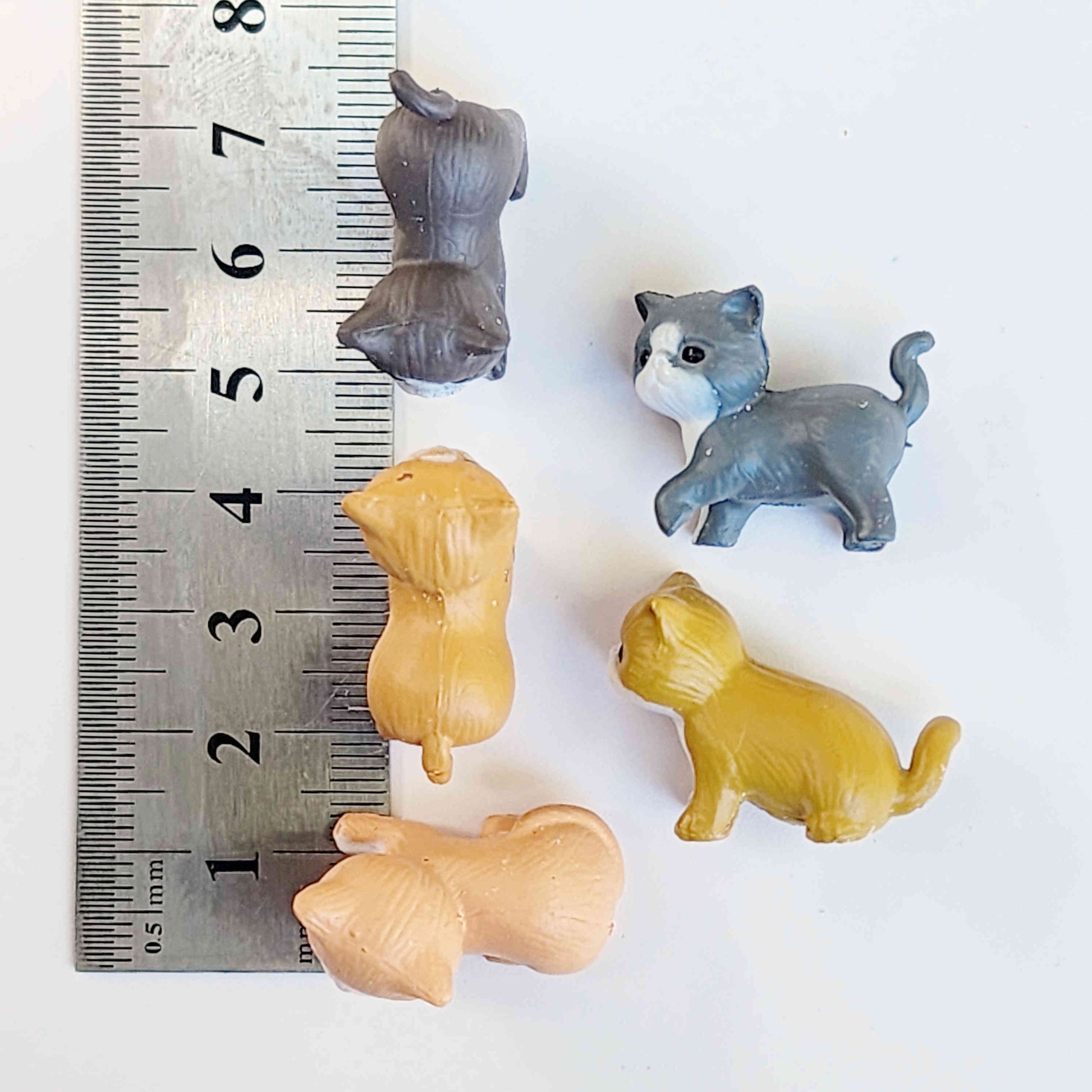 small PVC cat figurines on a white background next to a metal ruler