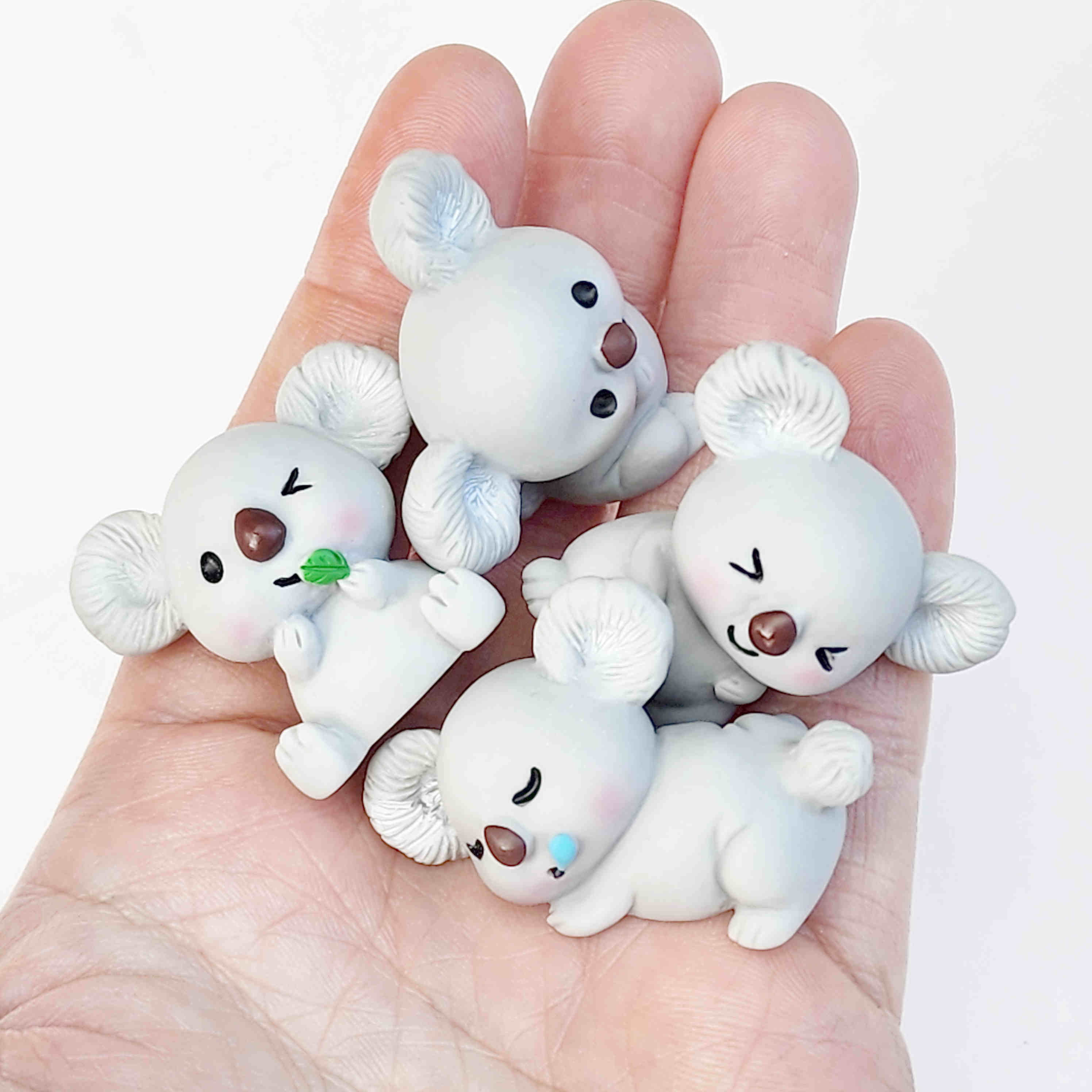 Cute grey koala resin figurines being held in the palm of a hand on a plain white background