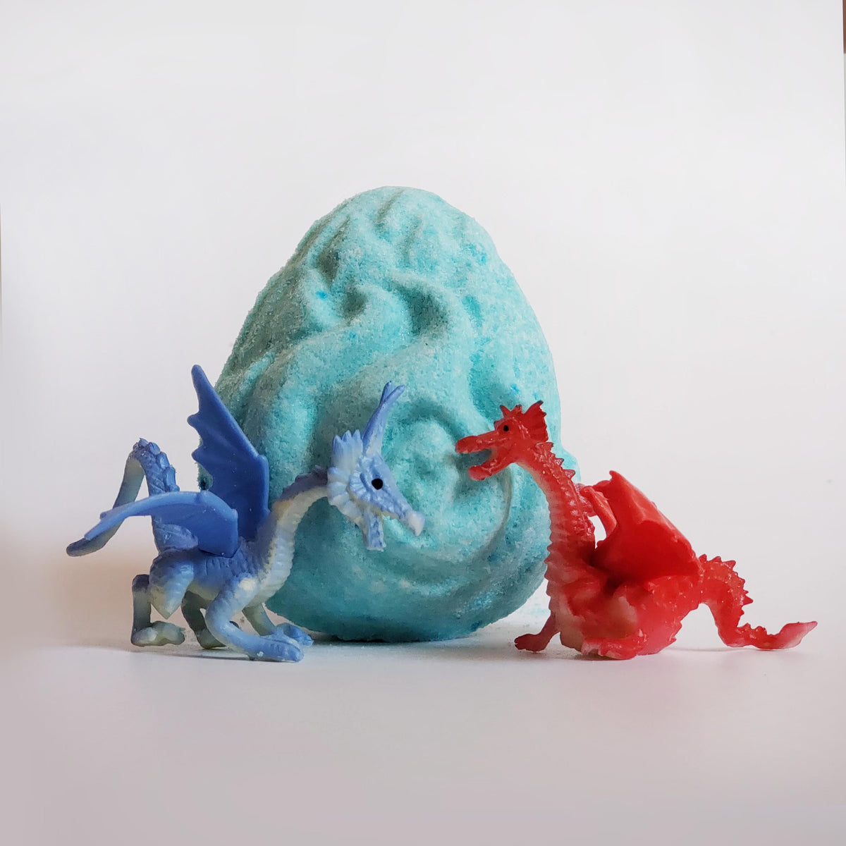 a blue and red dragon figurine placed in front of a teal egg shaped bath bomb