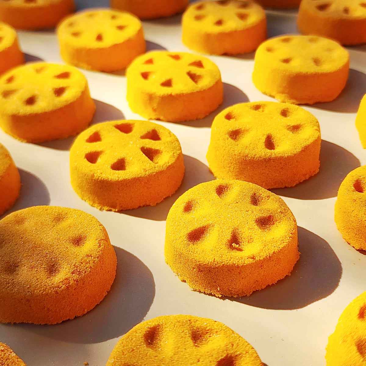 Orange slice shaped mini bath bomb layed out in an array across a plain neutral background