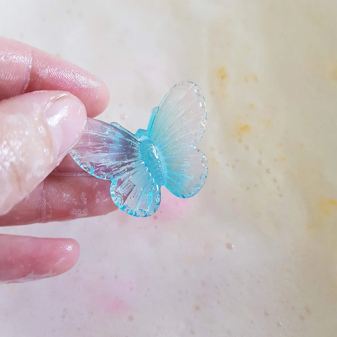 transparent blue butterfly charm being held over bath tub water