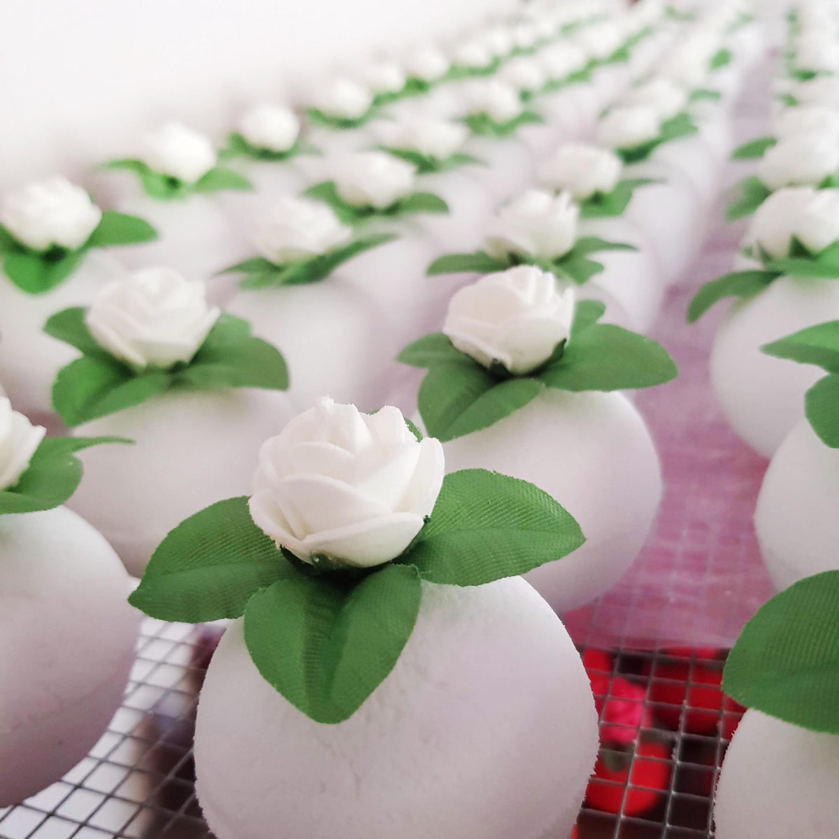 rows of white round bath bombs with jasmine flowers on top placed on a wire rack