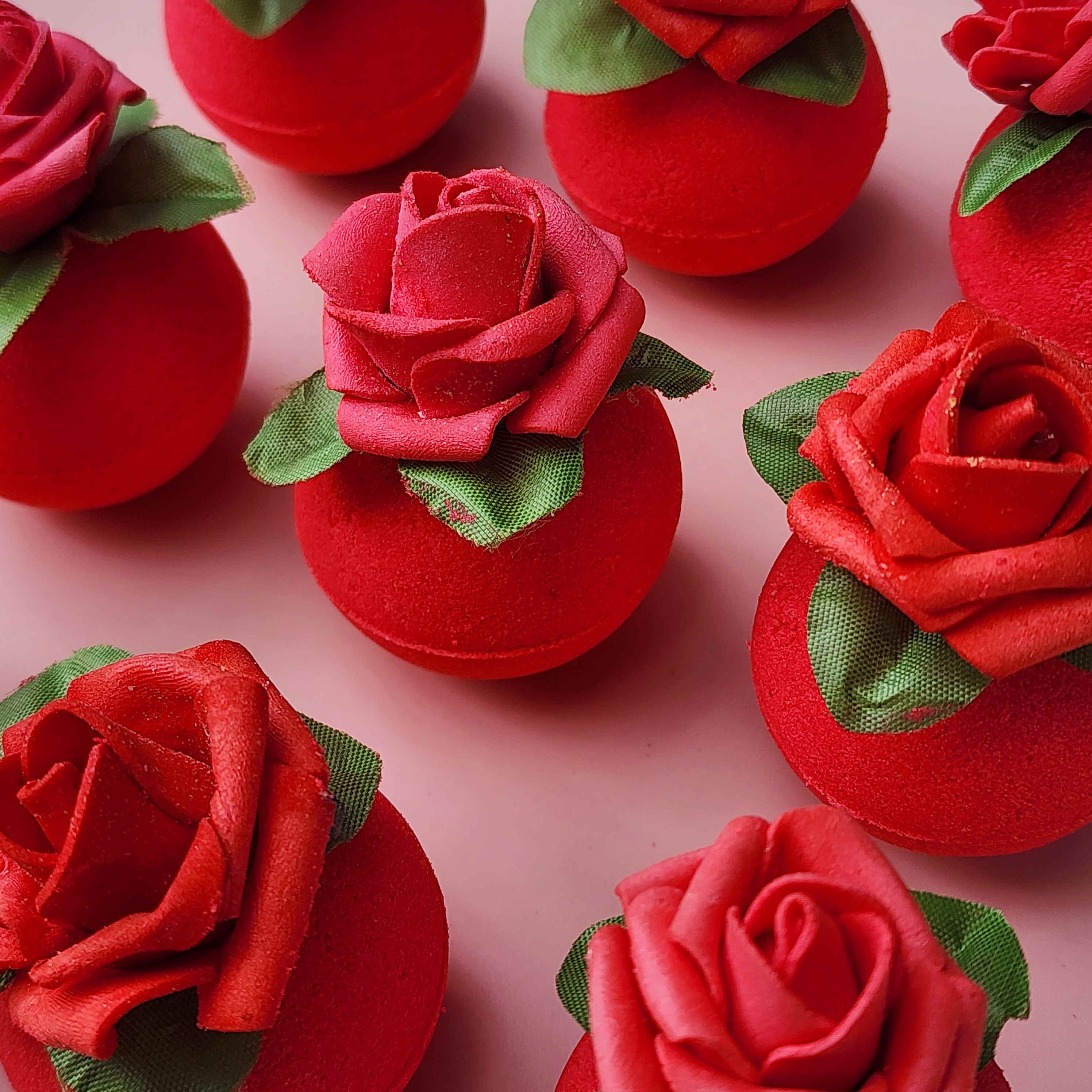 Red circular bath bomb with a rose on top on a pink background