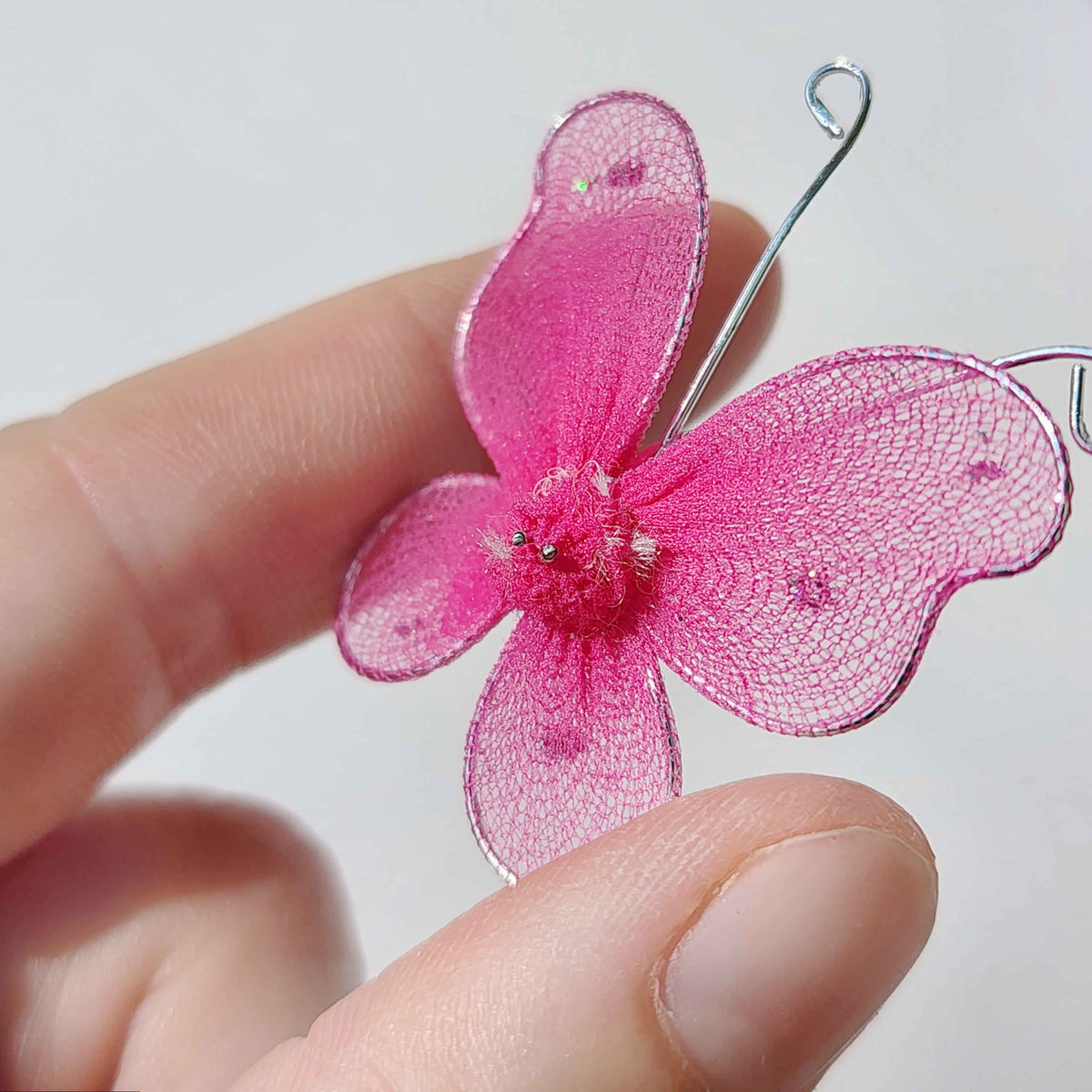 pink butterfly made of mesh fabric and wire being held in a hand on a white background