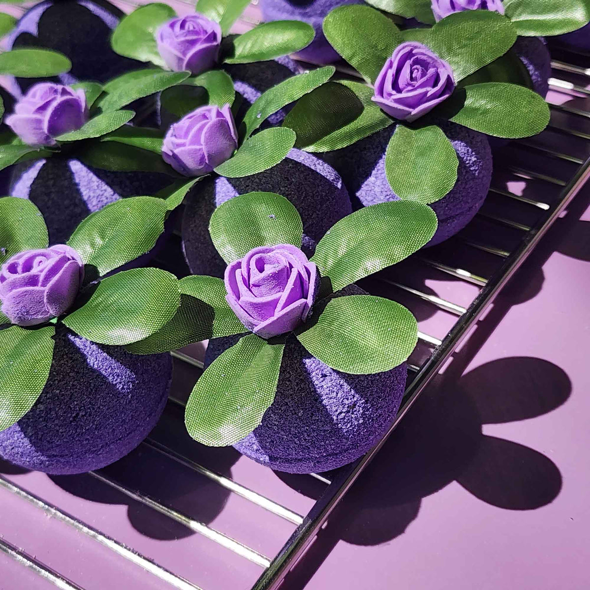 Close-up of Wild Berry bath bombs with green leaves and violet roses on a tray