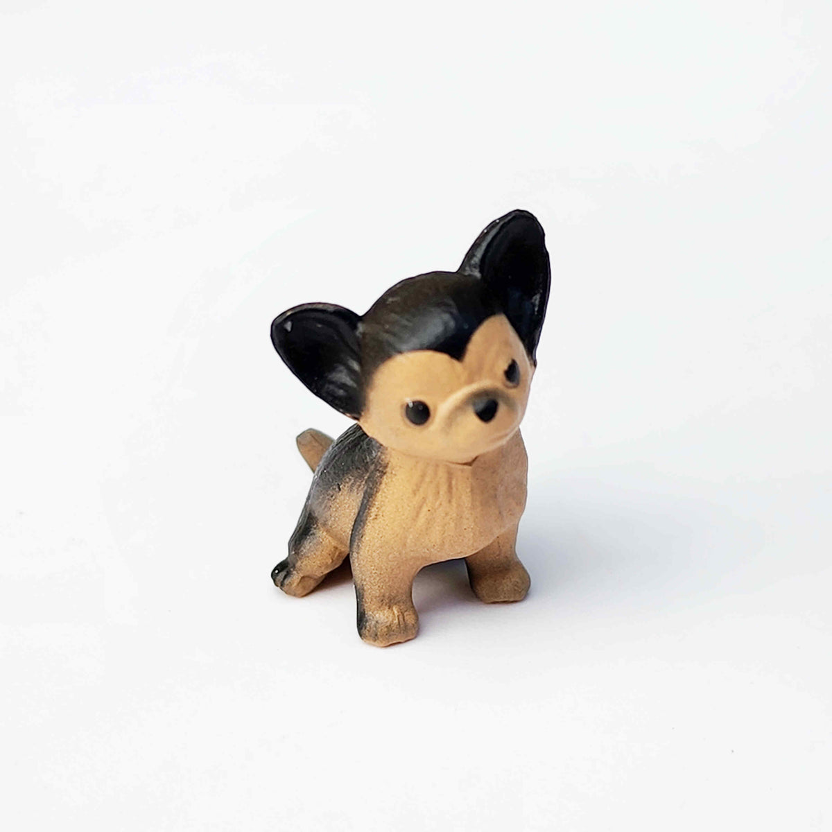 a black and brown chihuahua figurine sitting on a plain white background
