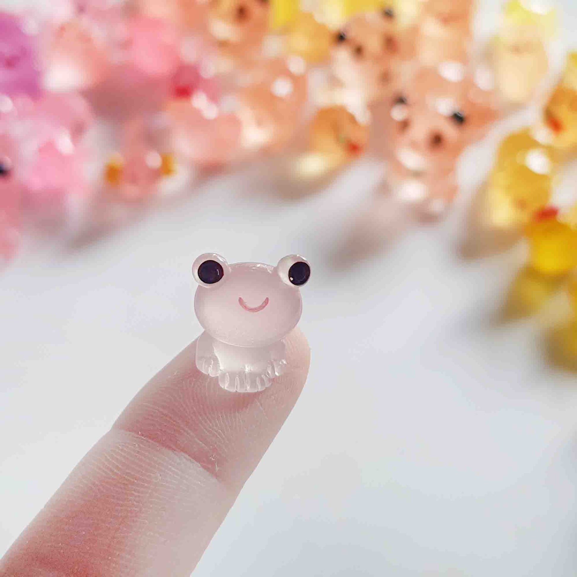Tiny translucent frog fairy garden toy held on one finger