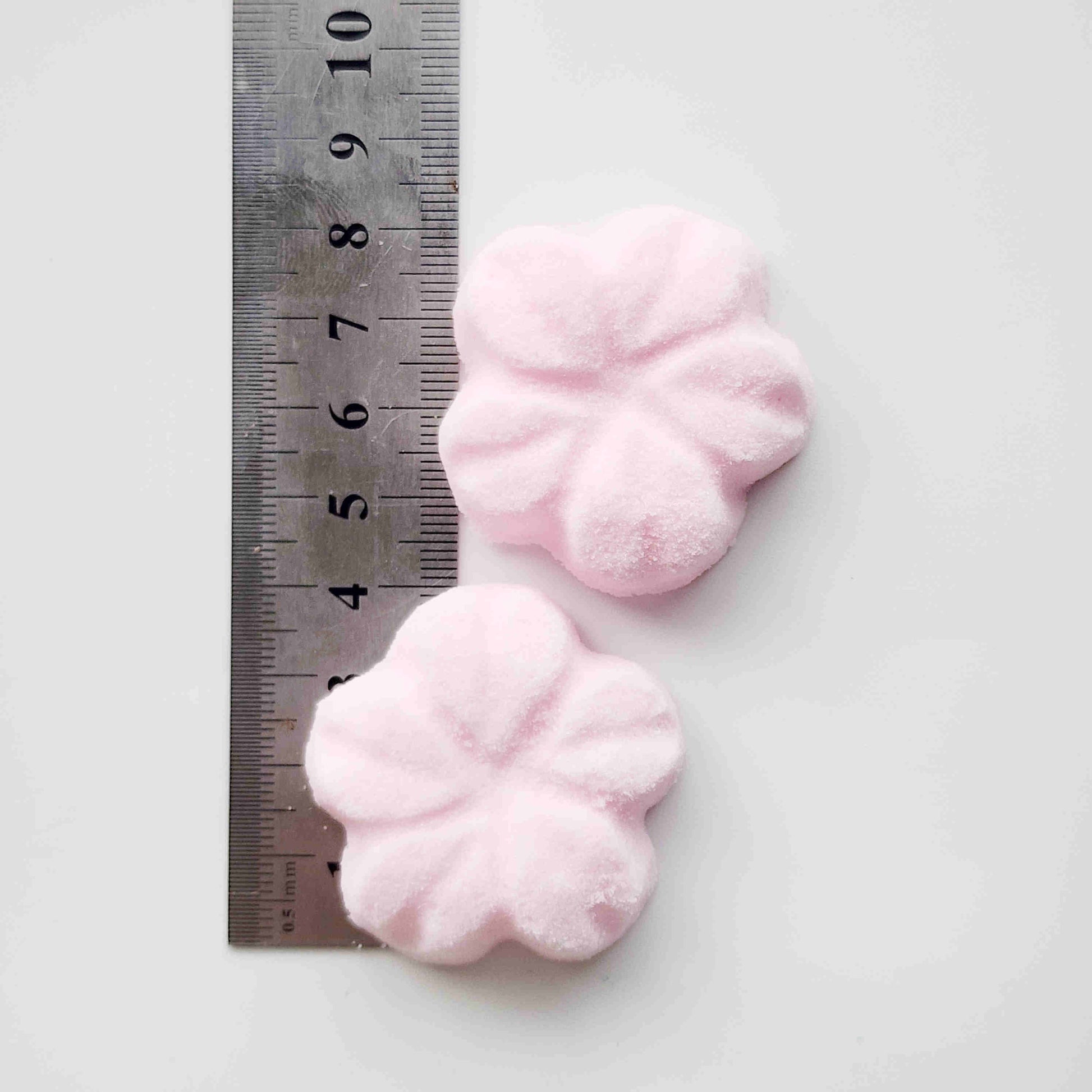 5 petal cherry blossom shaped bath bombs coloured light pink on a white background by a metal ruler