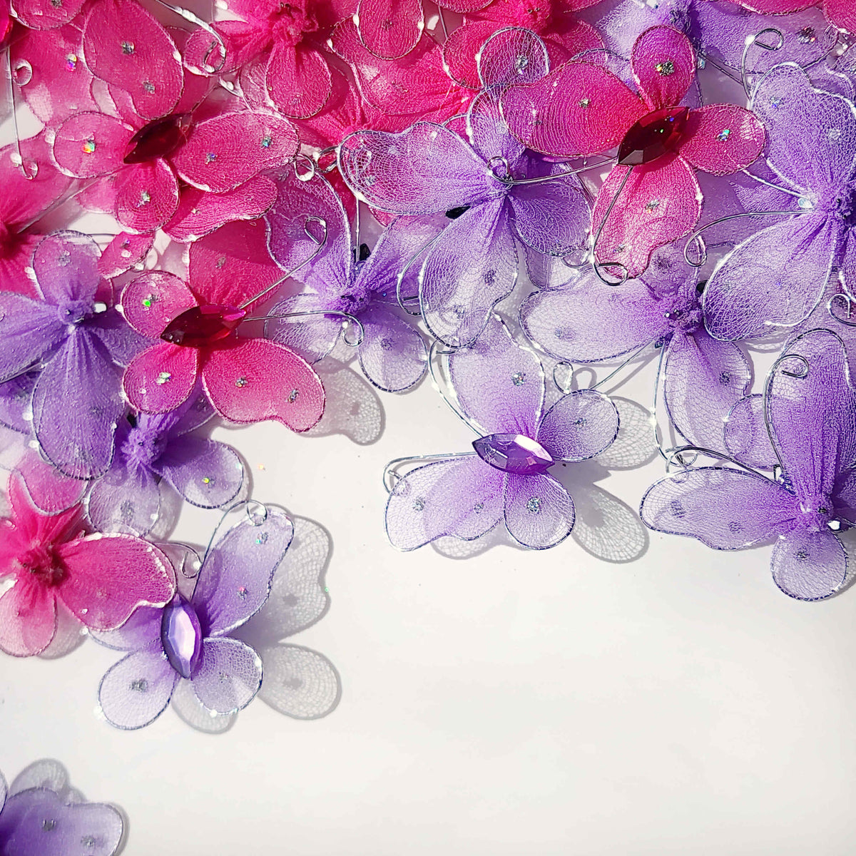 scattered pink and purple butterflies made of mesh fabric and wire on a white background